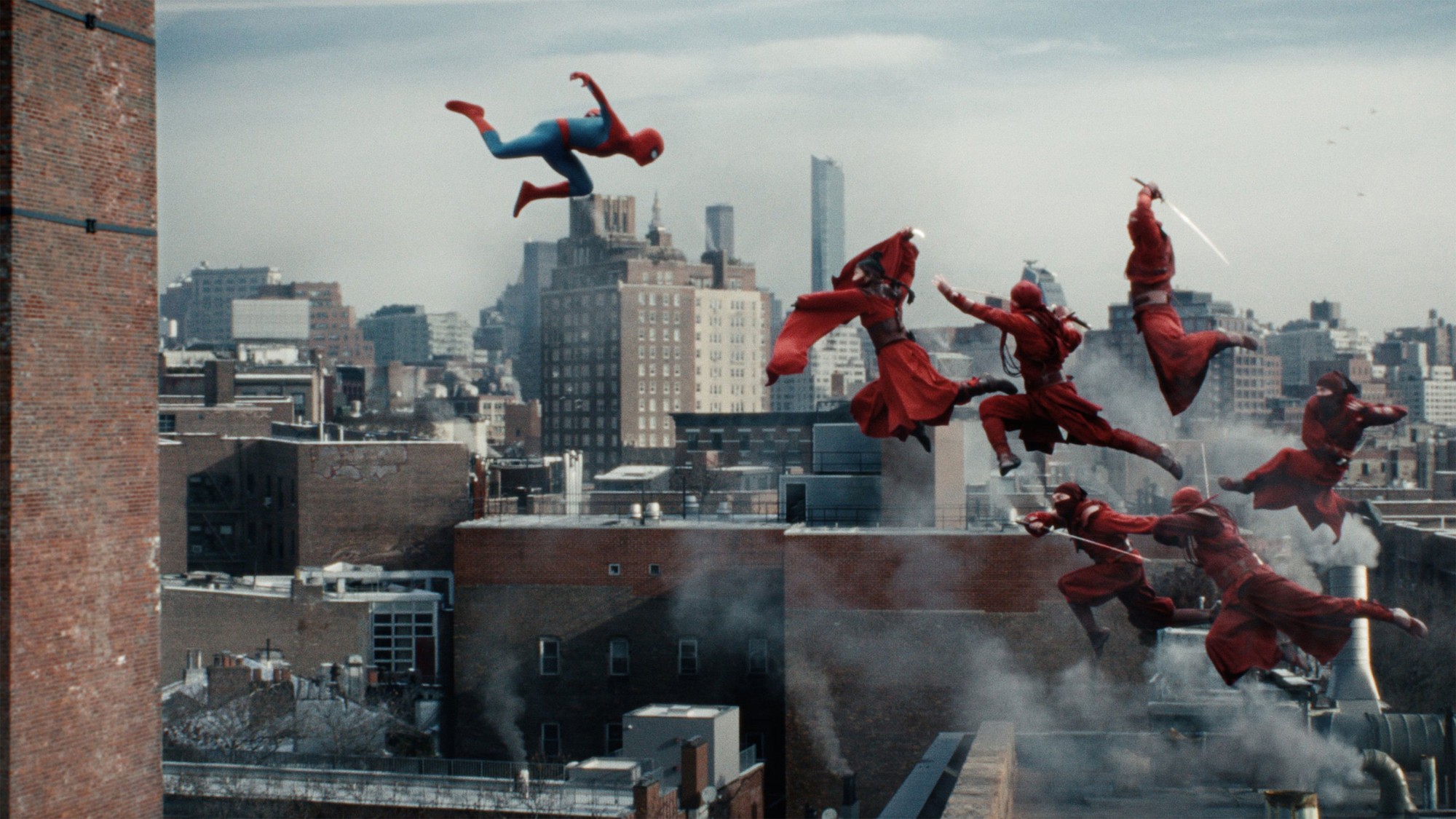 Peter Parker salta desde una azotea de Nueva York hacia un grupo de enemigos vestidos de rojo en pleno combate