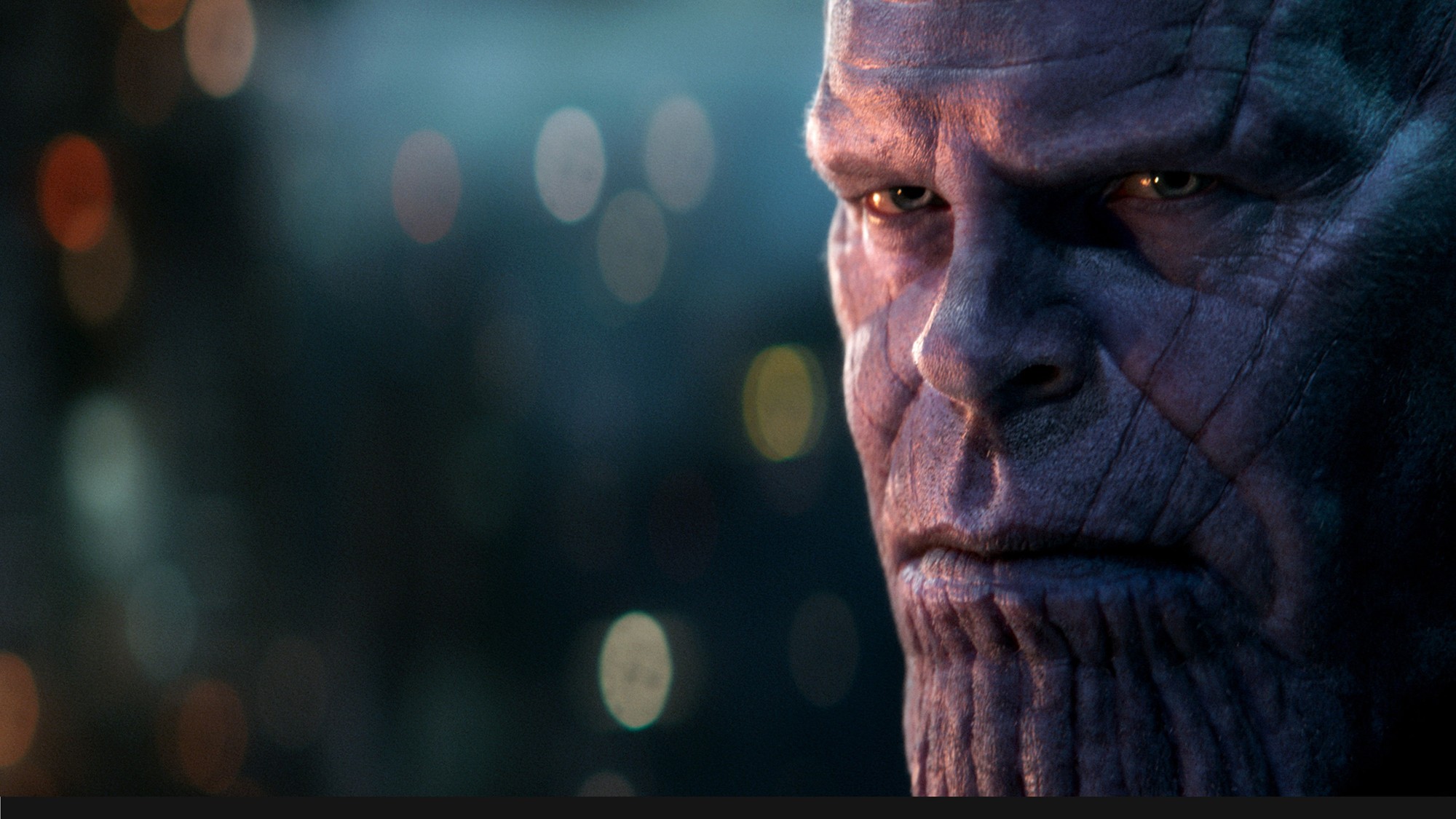 Primer plano del rostro de Thanos, el Titán Loco, iluminado en tonos azules sobre un fondo desenfocado con luces de colores