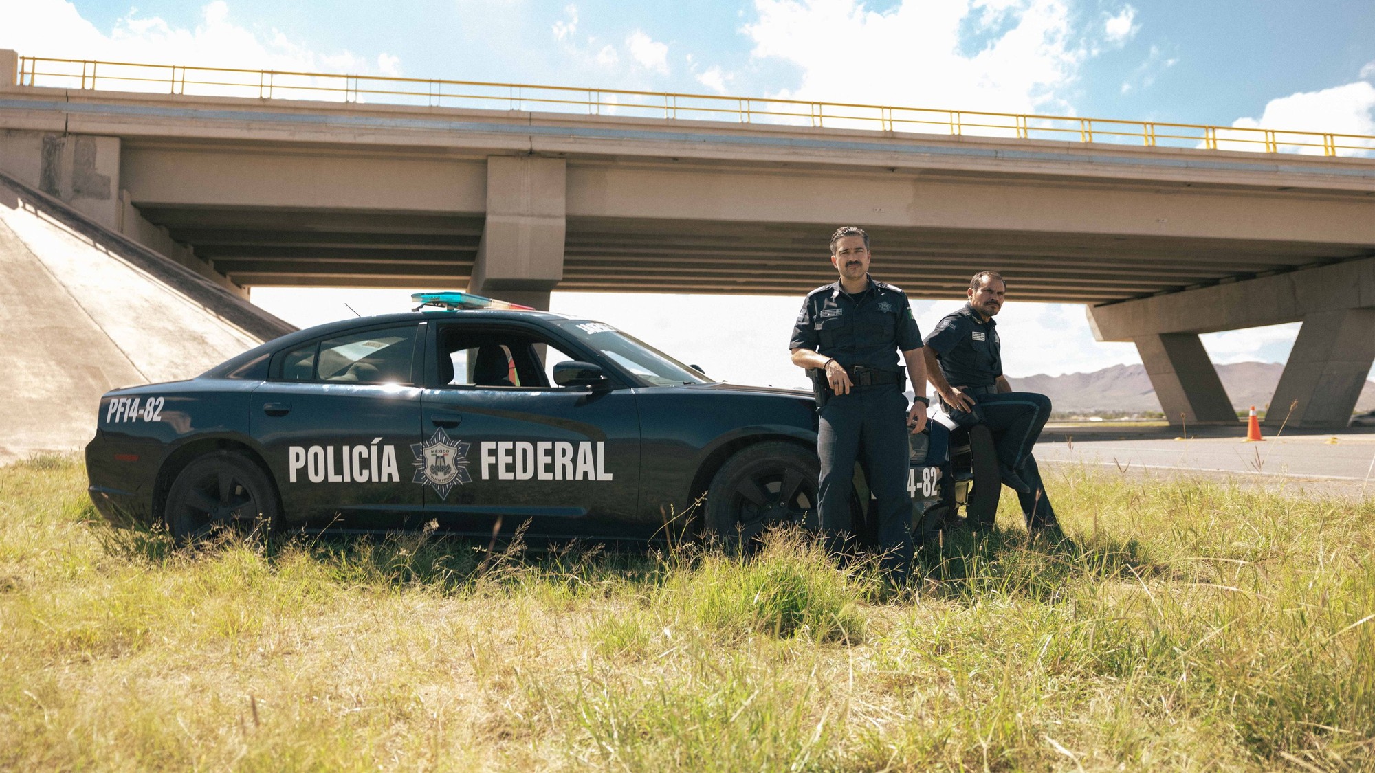 Dos policías federales recargados en una patrulla estacionada bajo un puente en una carretera del norte de México