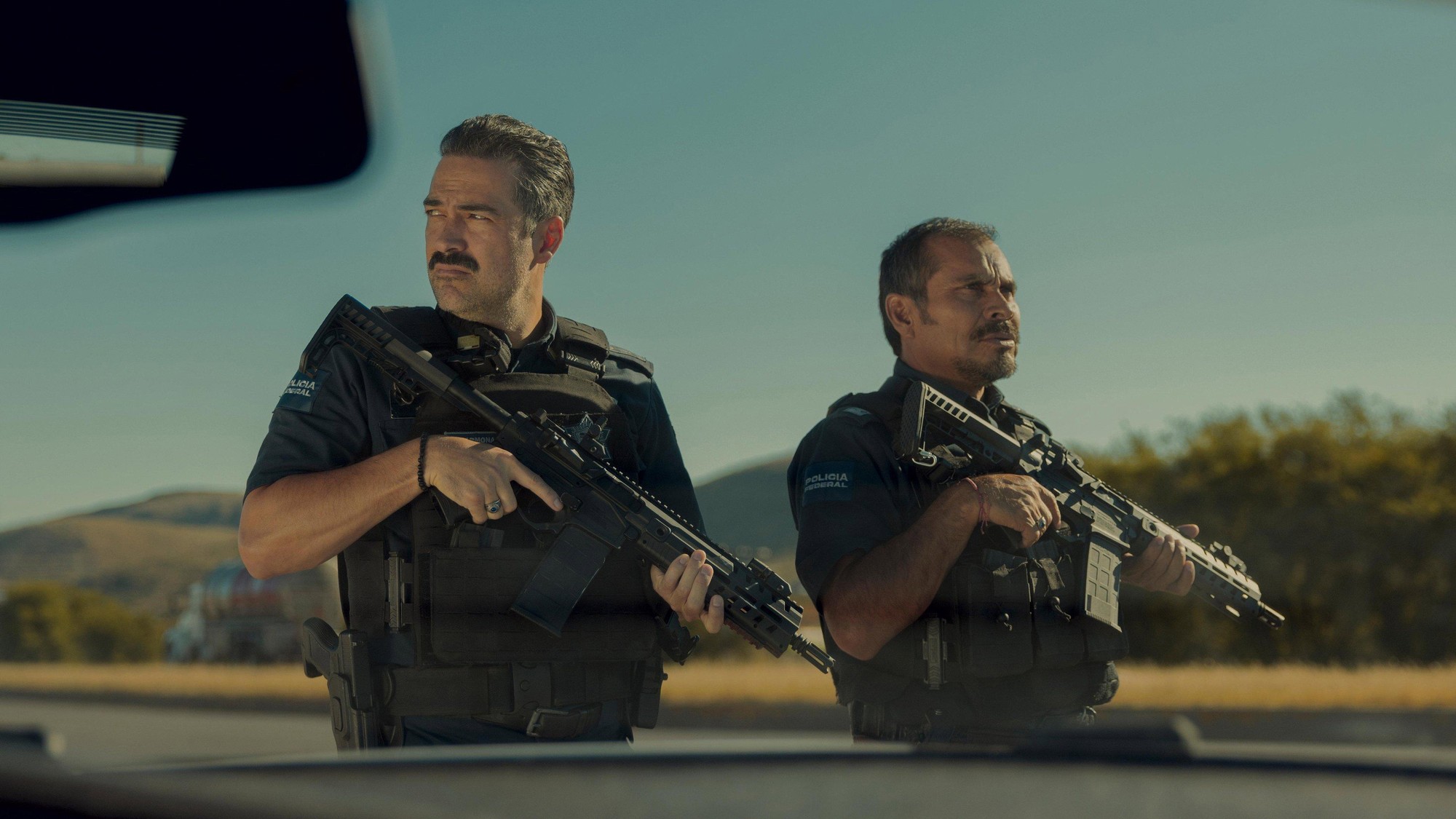 Los dos agentes federales empuñan sus rifles y vigilan la carretera, vistos a través del parabrisas de su vehículo