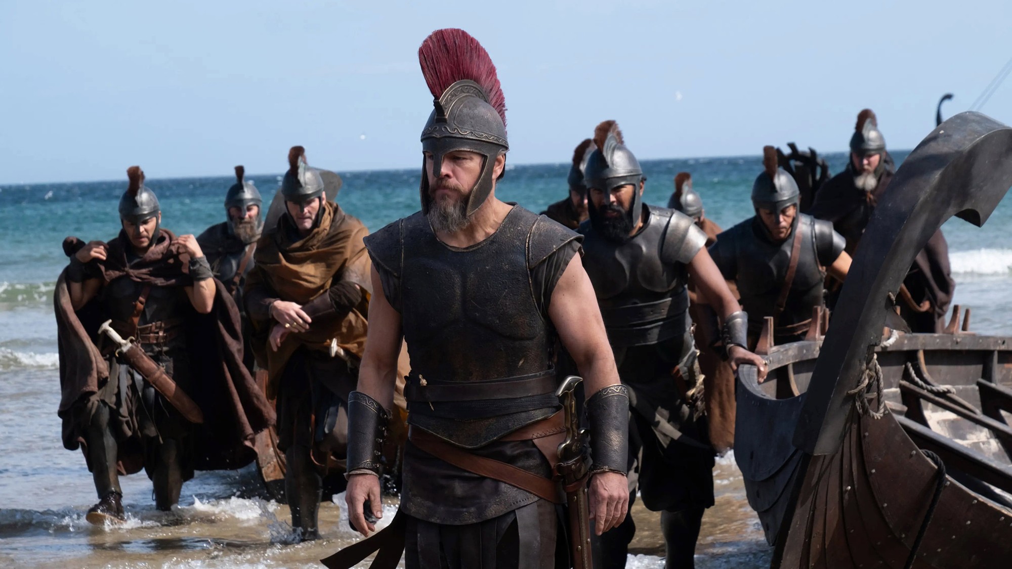 Odiseo y sus hombres desembarcan de una embarcación de madera en una playa soleada en The Odyssey