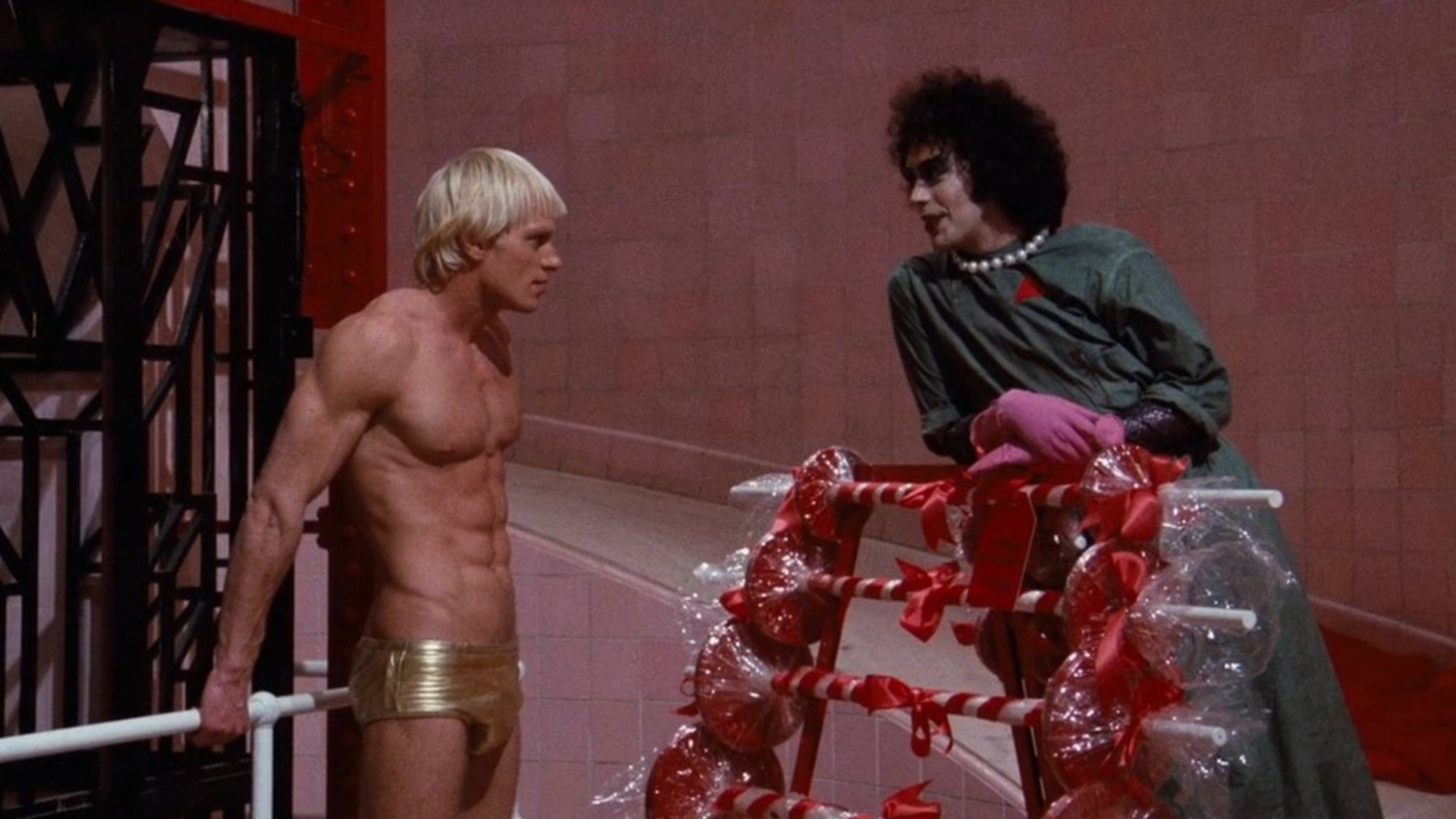 Tim Curry, caracterizado como el doctor Frank-N-Furter, conversa con Rocky en el laboratorio de la mansión en The Rocky Horror Picture Show