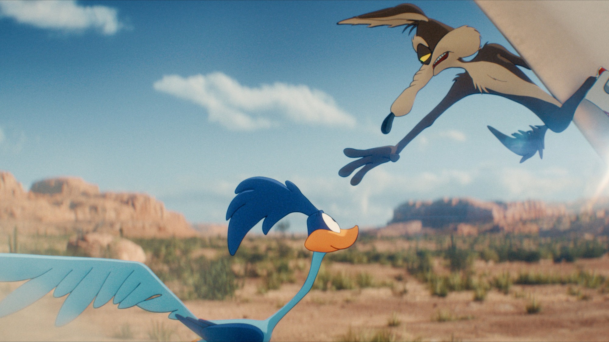 El Coyote se abalanza en el aire sobre el Correcaminos en pleno desierto de rocas rojas bajo un cielo azul despejado
