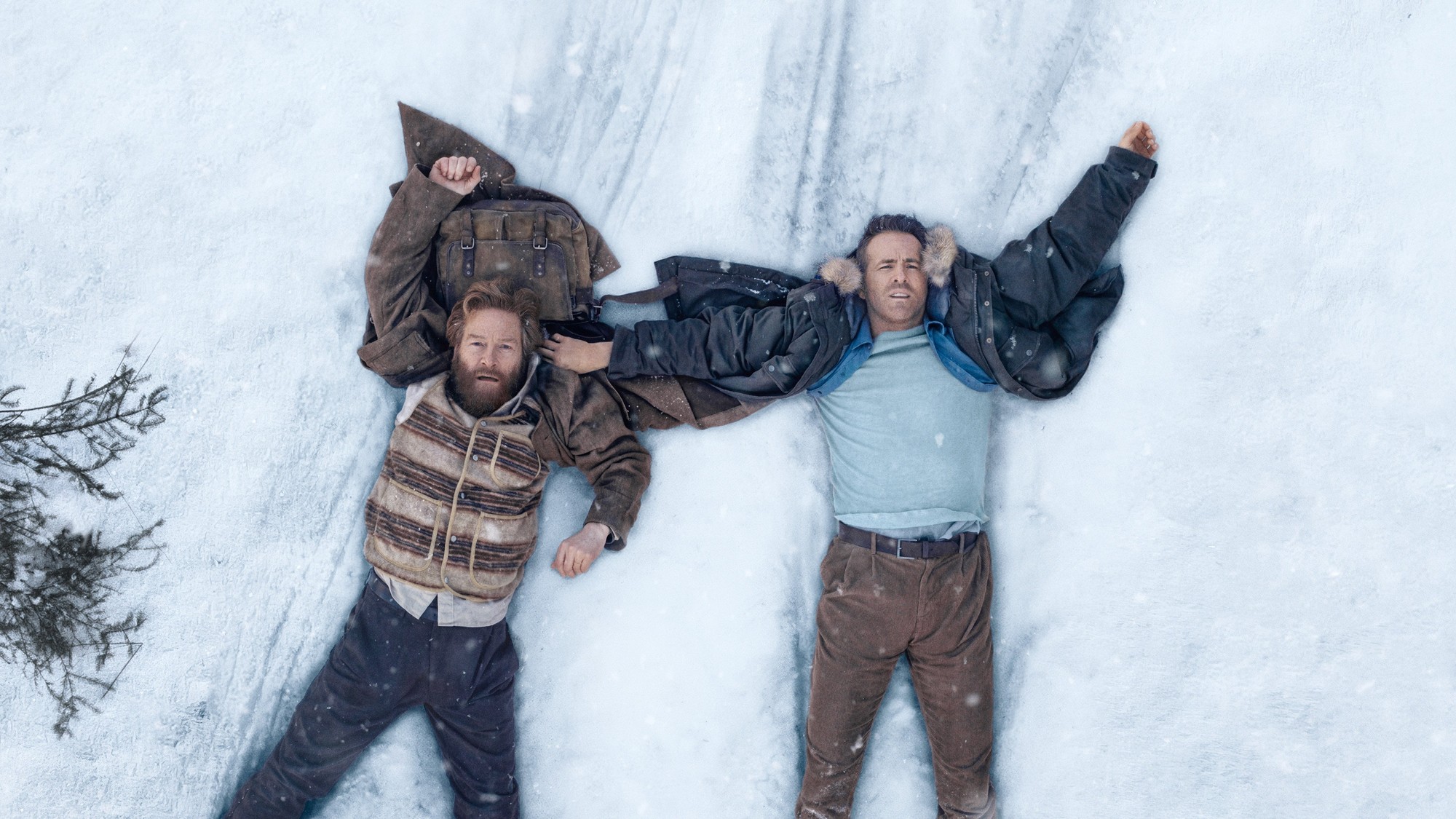 Vista cenital de Ryan Reynolds y Kenneth Branagh tendidos boca arriba sobre la nieve con los brazos extendidos, agotados tras la huida