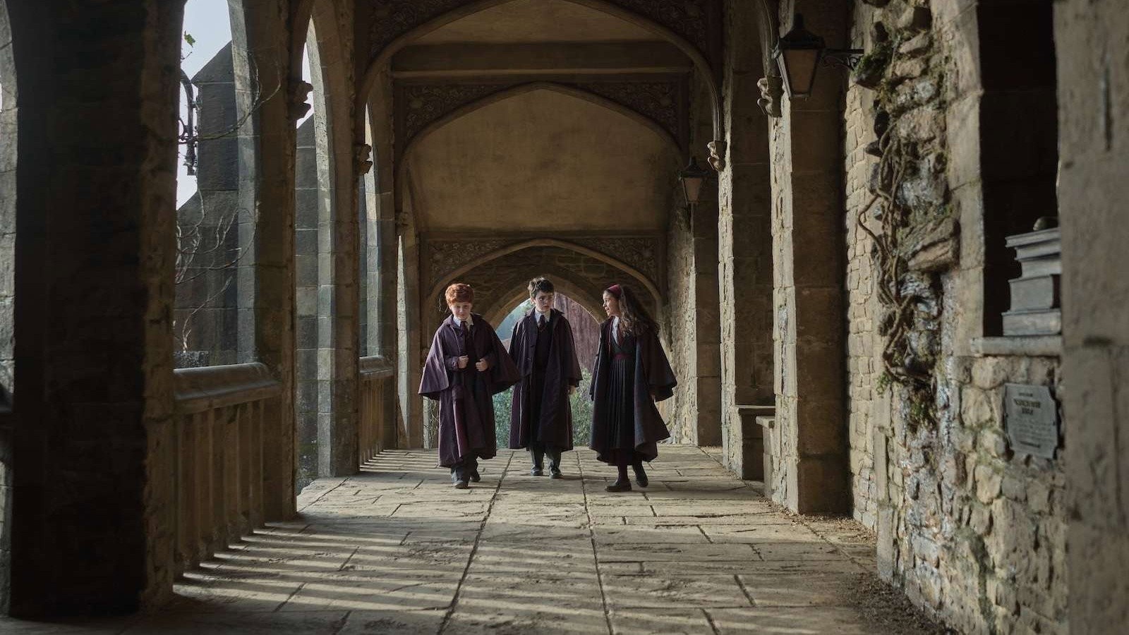 Tres alumnos de Hogwarts caminan con sus túnicas por un claustro de piedra en la serie de Harry Potter de HBO Max