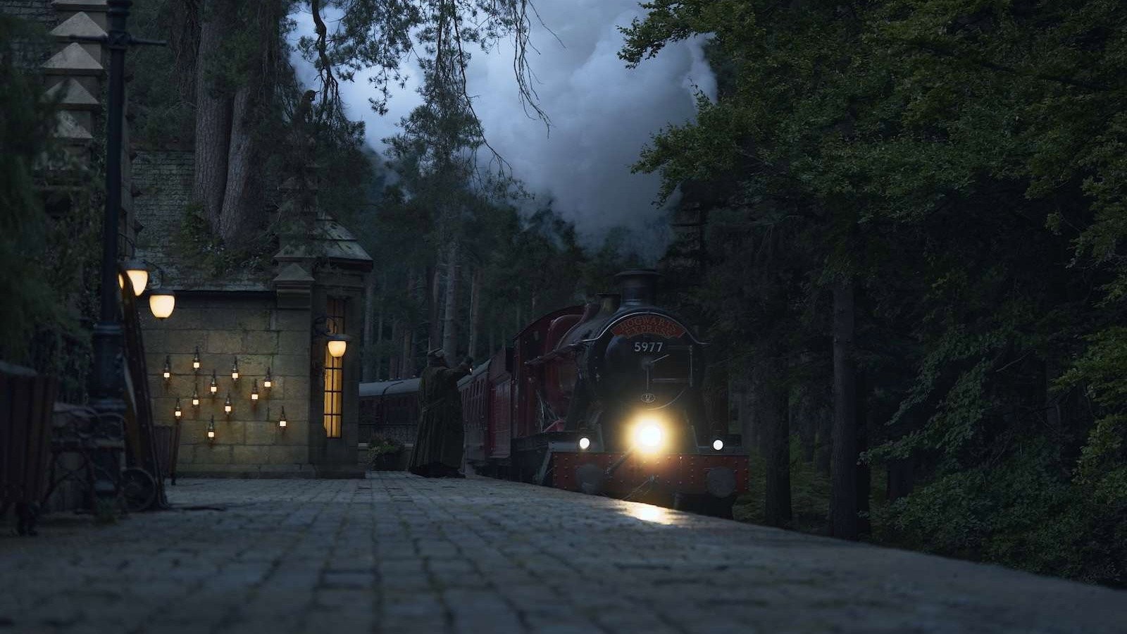 El tren de Hogwarts espera de noche en una estación rodeada de bosque, con las farolas encendidas, en la serie de HBO Max