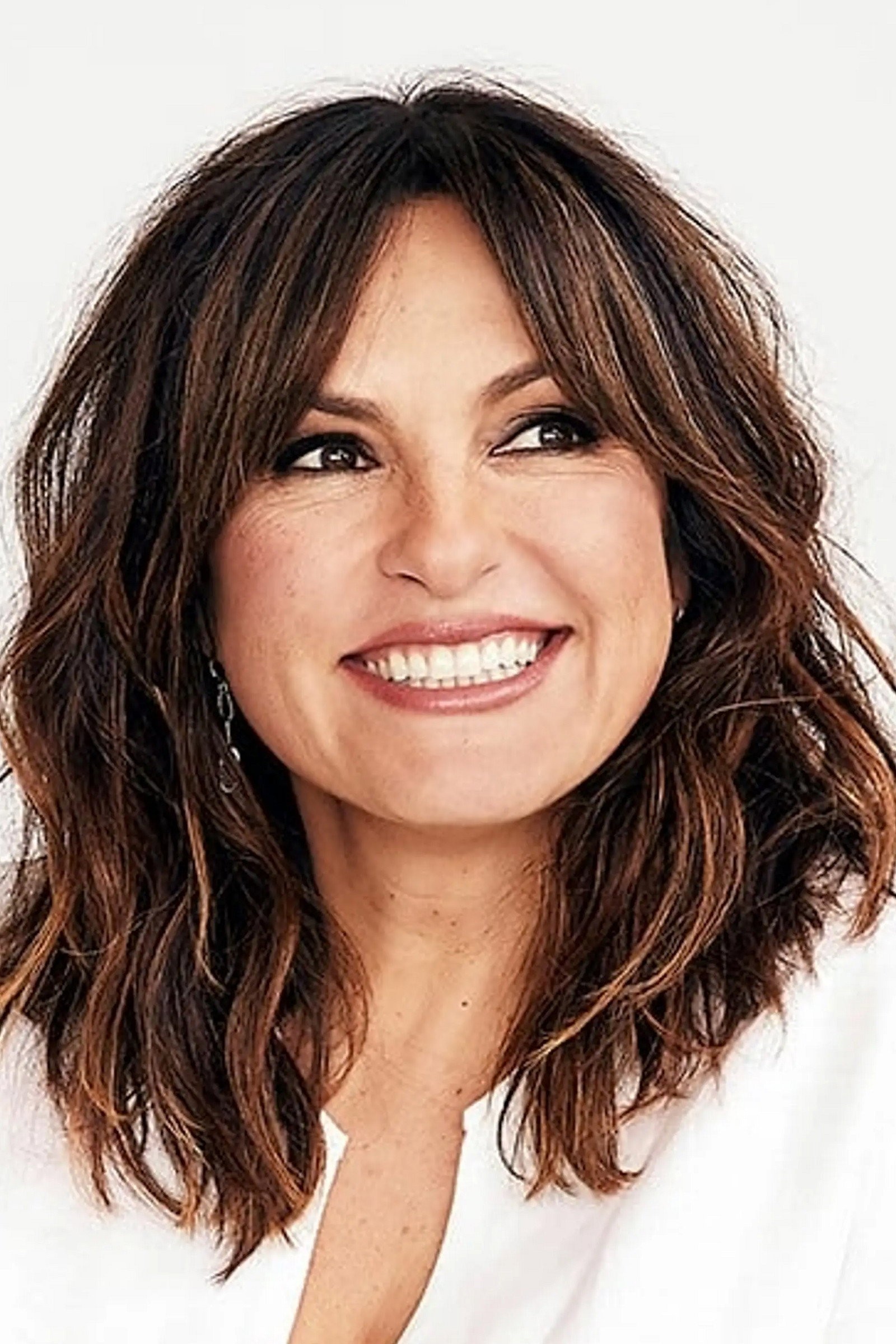 Retrato de Mariska Hargitay sonriendo sobre fondo blanco, con el cabello suelto y blusa clara