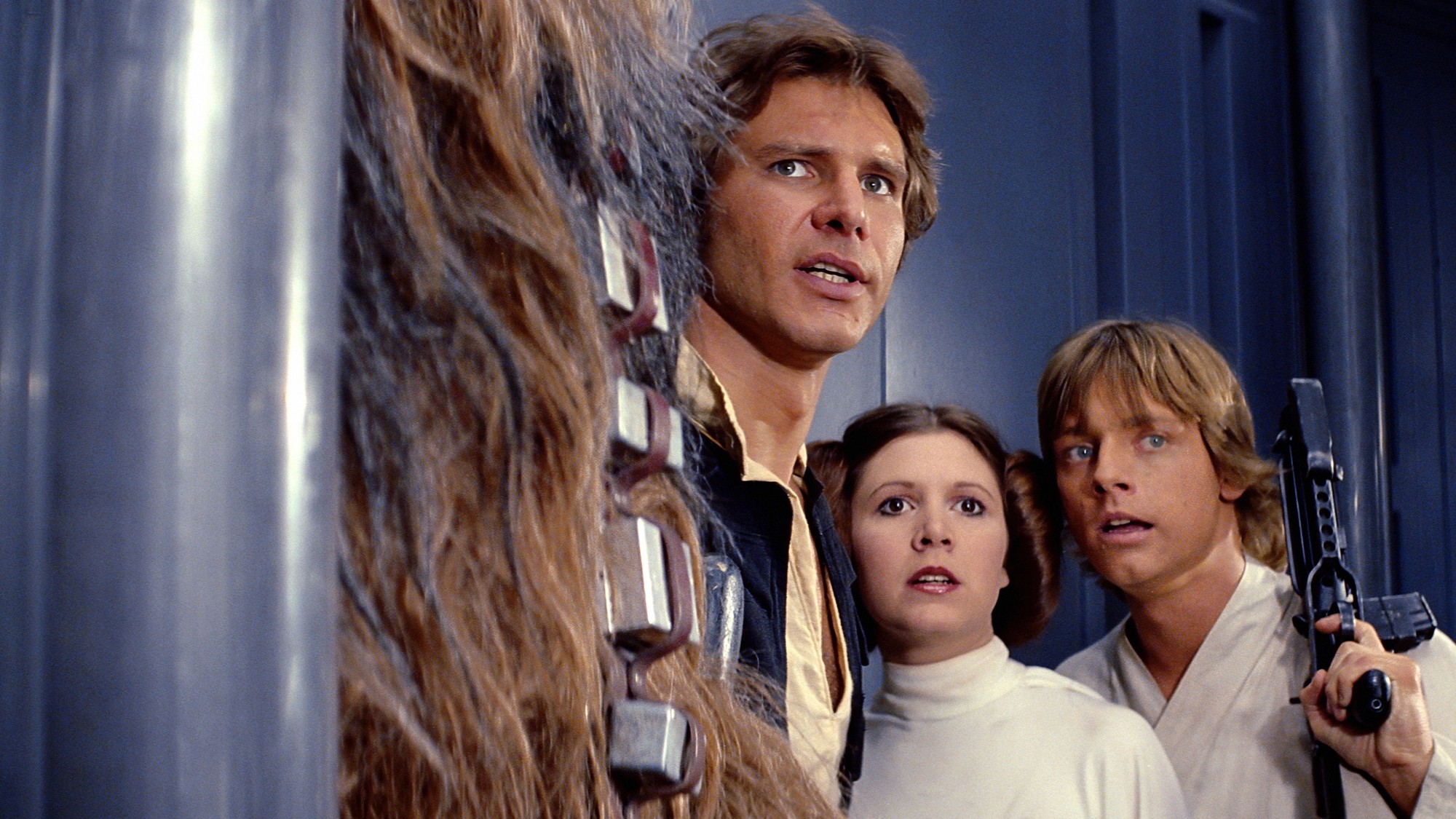 Han Solo, la princesa Leia, Luke Skywalker y Chewbacca observan con alarma desde un pasillo metálico de la Estrella de la Muerte
