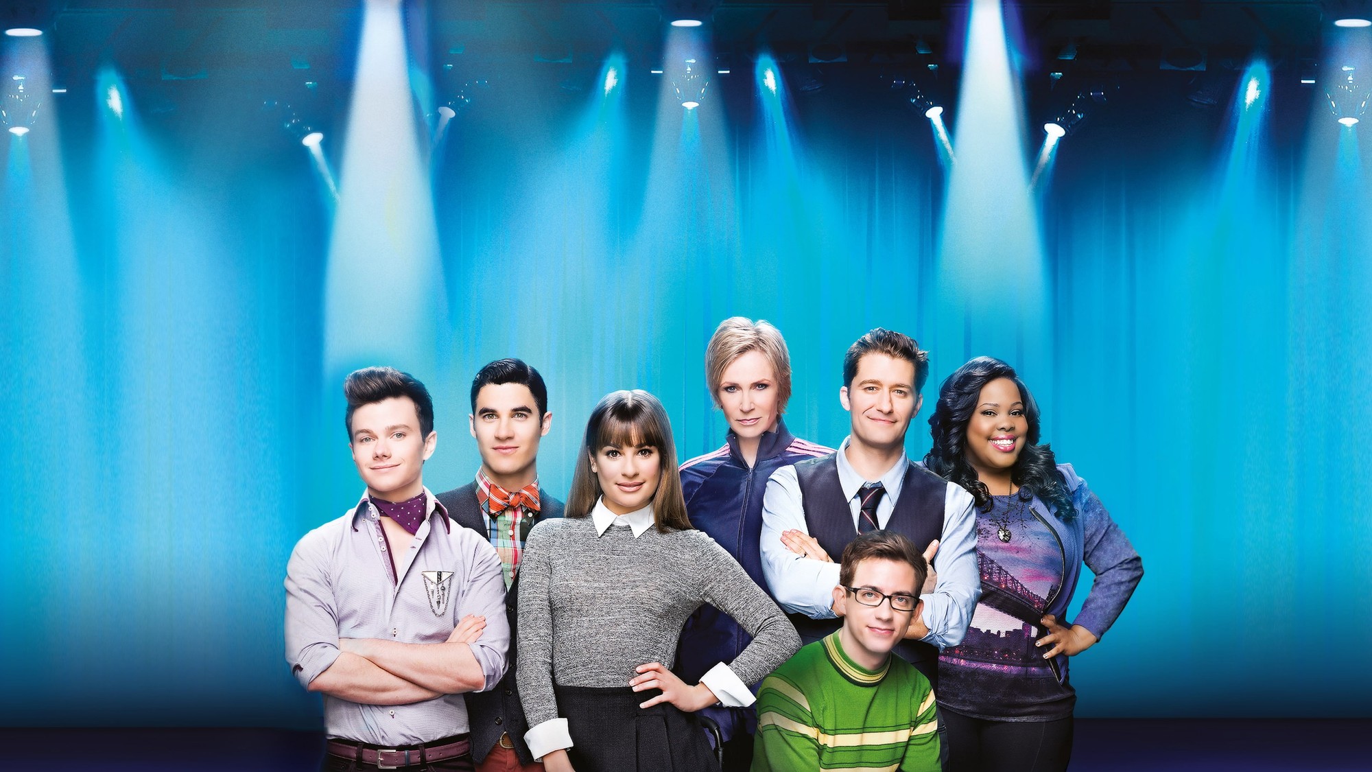 El elenco de Glee posando sobre un escenario iluminado con focos azules