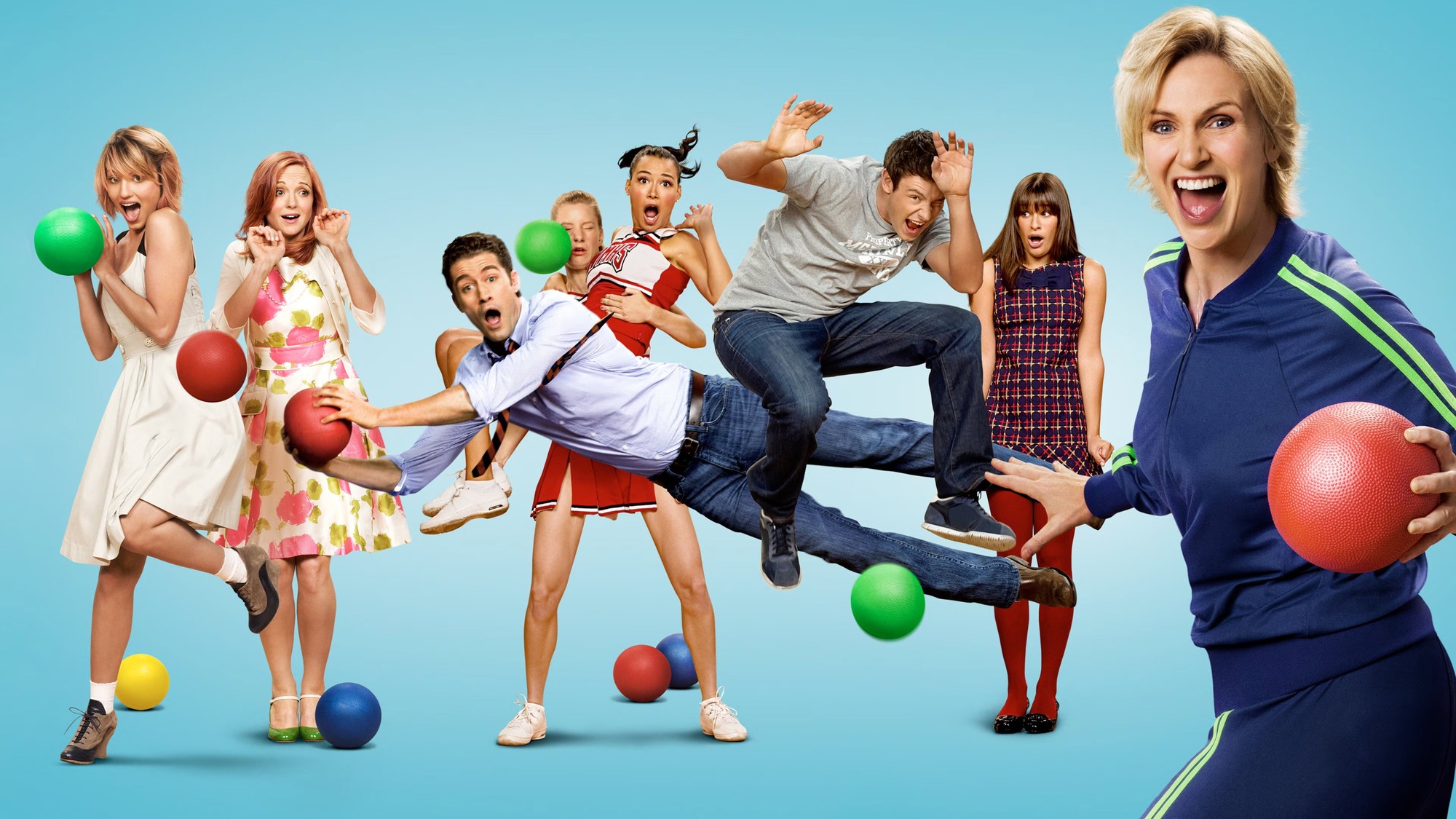 Jane Lynch como la entrenadora Sue Sylvester frente al reparto de Glee en una escena de comedia con pelotas de colores