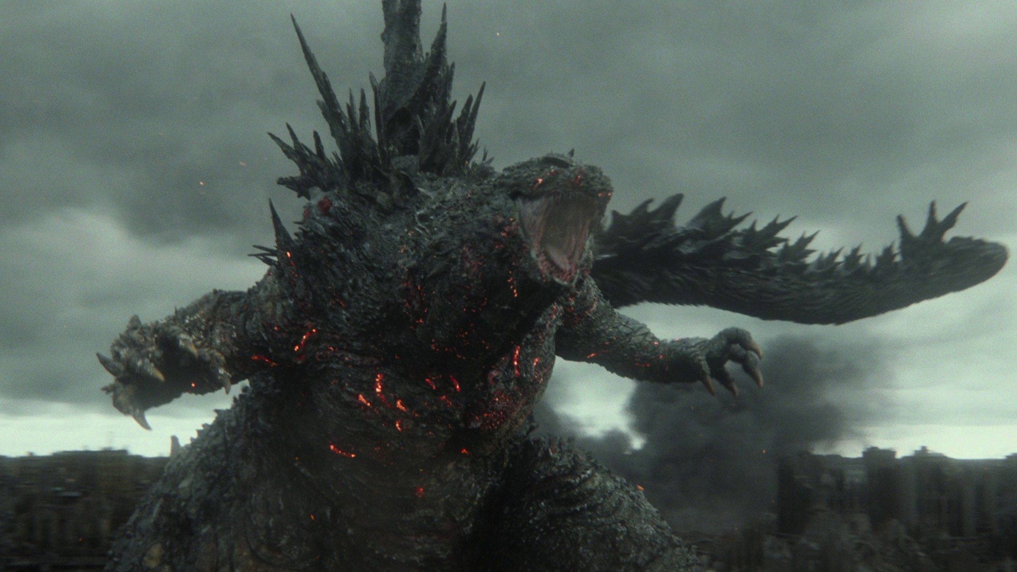 Godzilla ruge entre ruinas y humo mientras avanza sobre una ciudad devastada