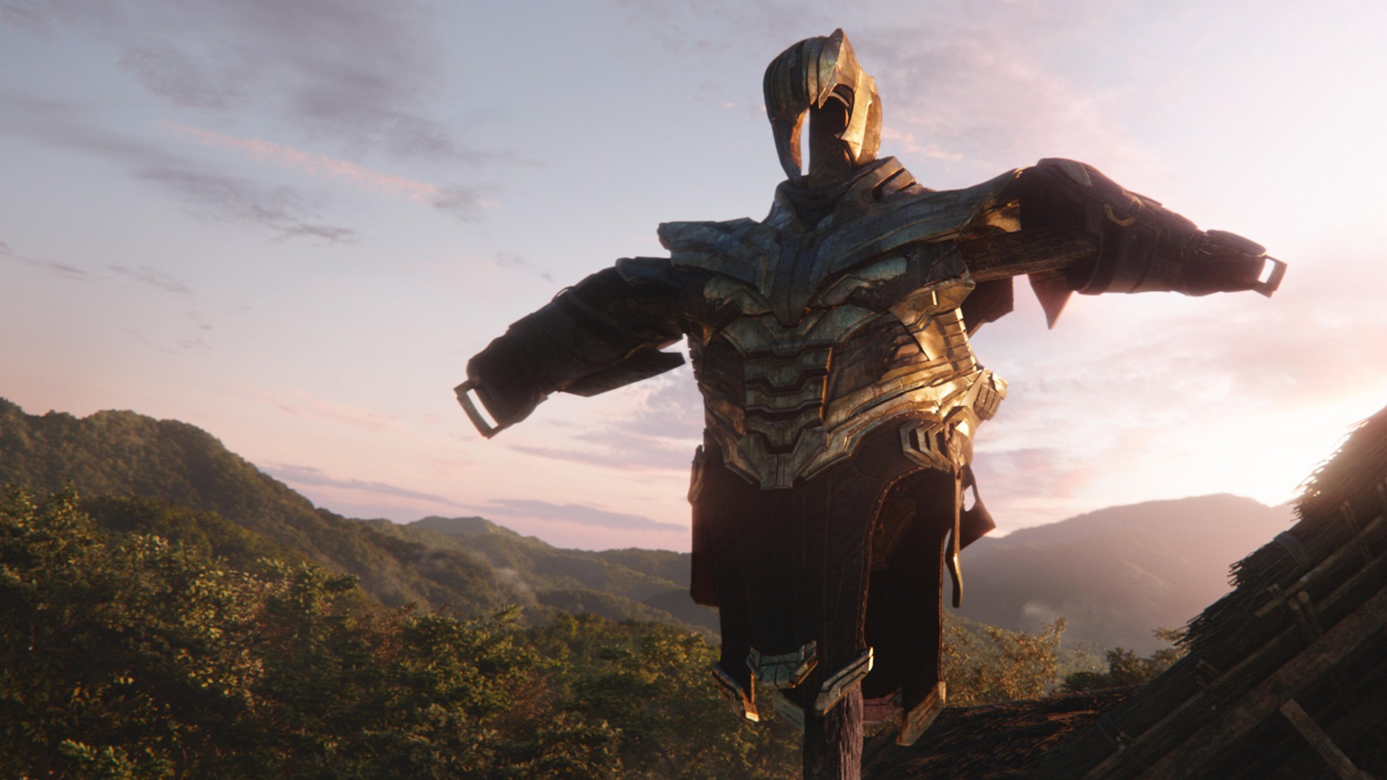 La armadura vacía de Thanos colgada como espantapájaros sobre un campo de cultivo, con montañas verdes al atardecer