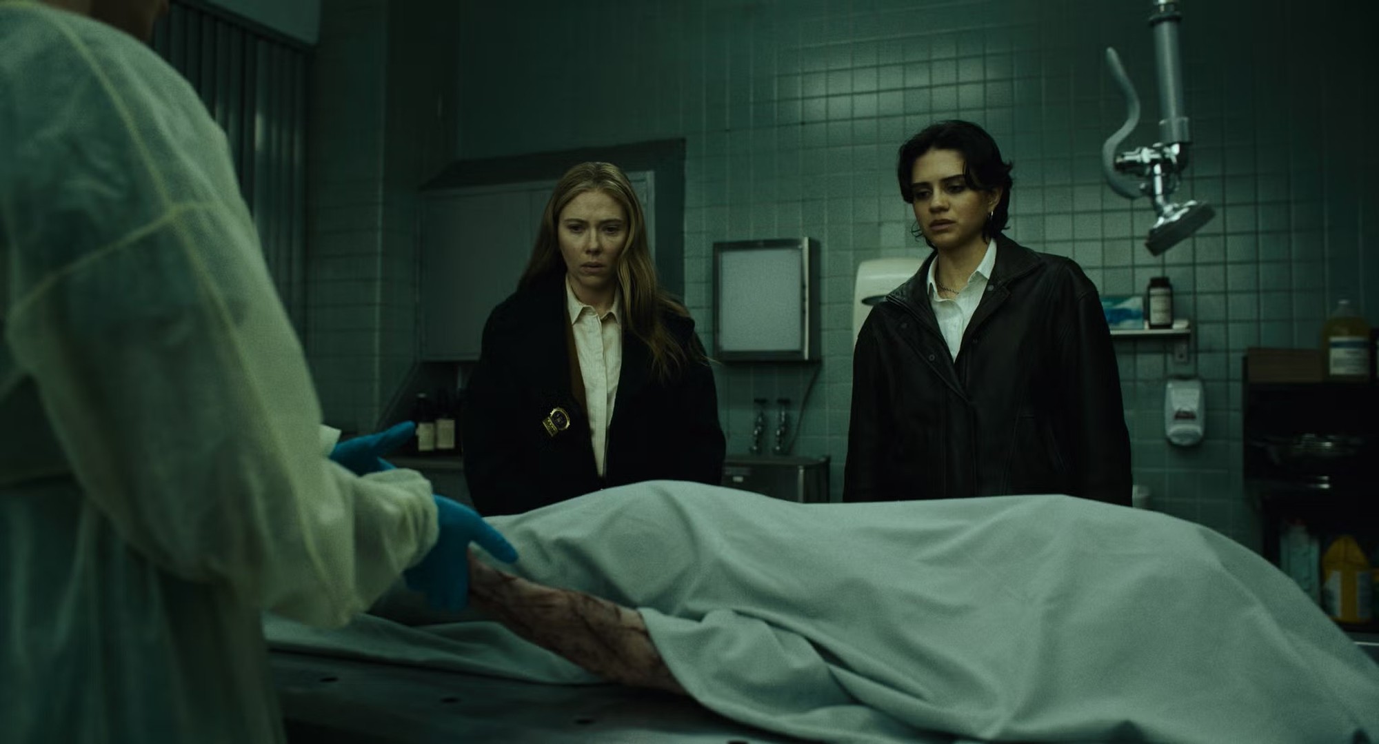 Scarlett Johansson y Sasha Calle observan un cuerpo cubierto con una sábana sobre la mesa de una morgue en The Exorcist: Martyrs