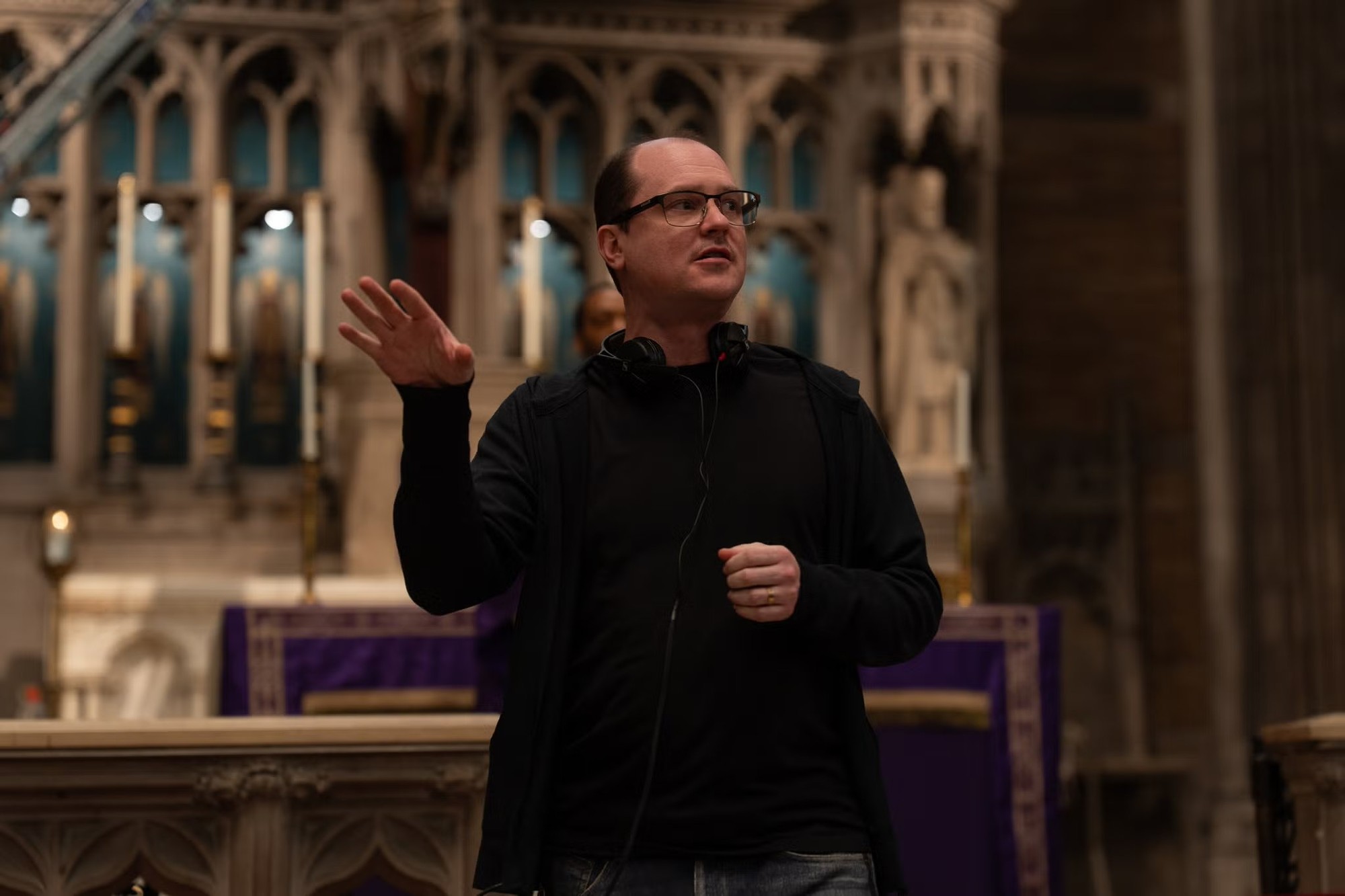 El director Mike Flanagan da indicaciones en el set de The Exorcist: Martyrs, frente al altar de una iglesia con velas y paños morados