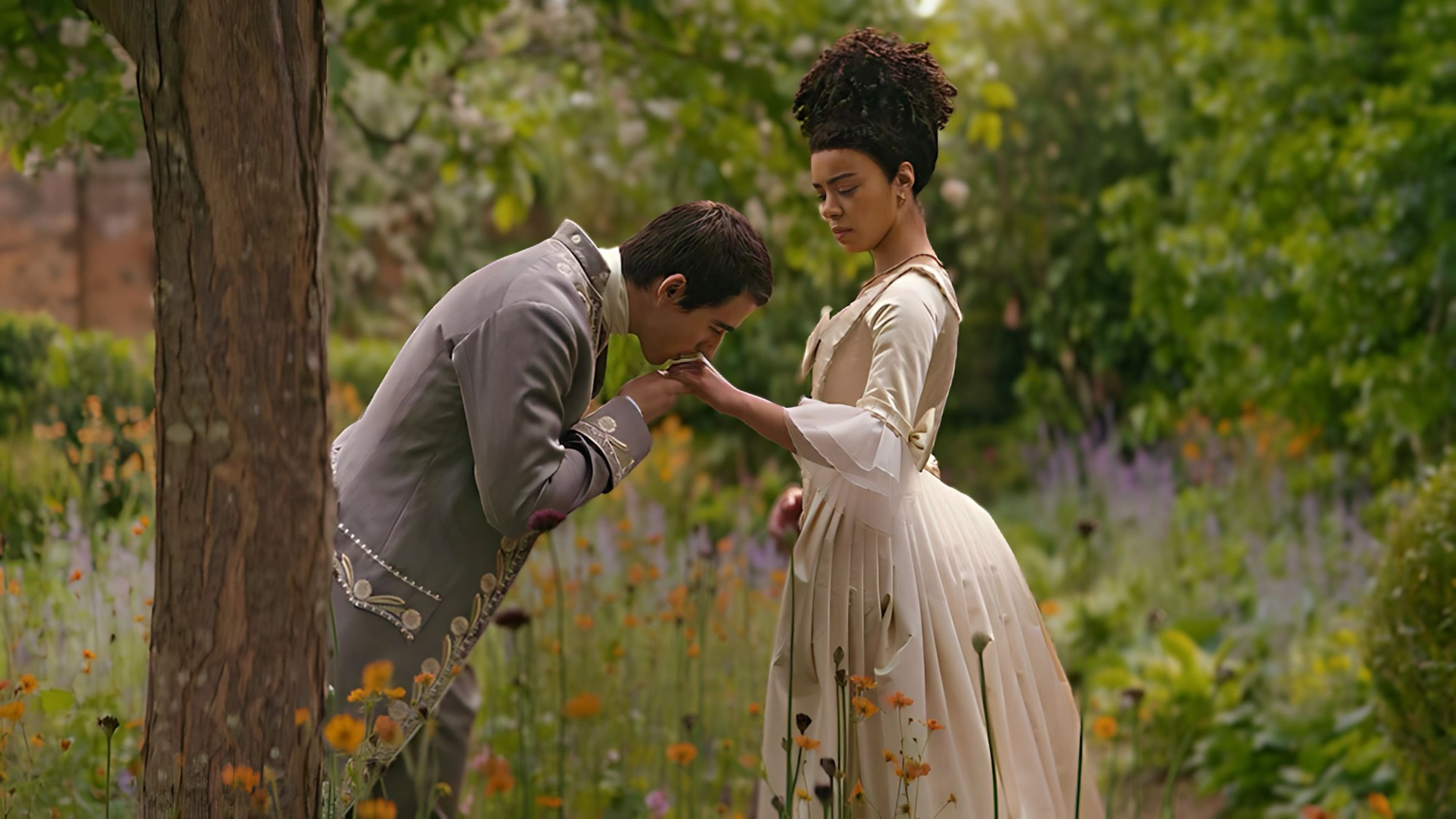 La joven reina Carlota y el rey Jorge en un jardín florido en la serie Queen Charlotte de Netflix