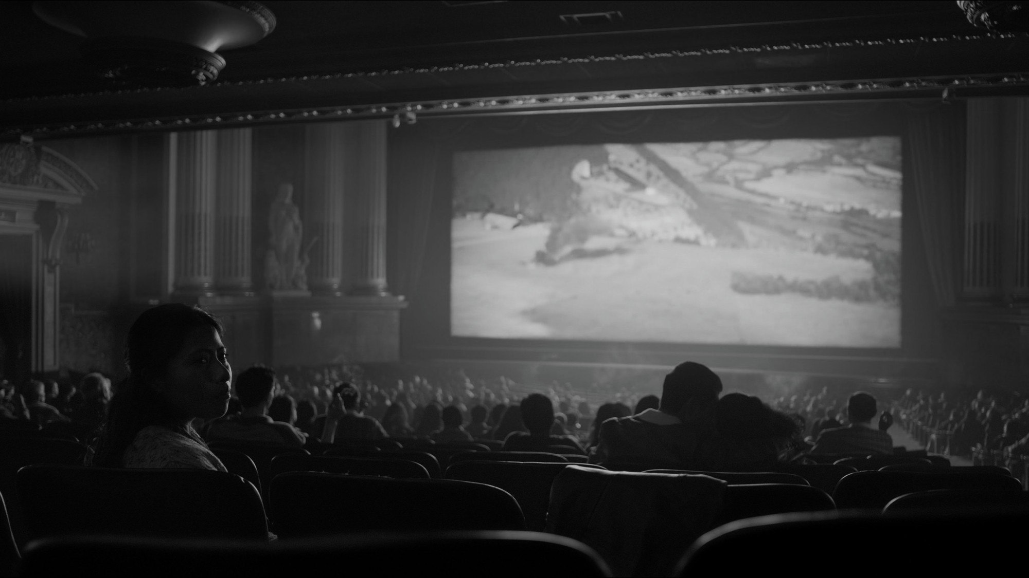 Público sentado en una gran sala de cine clásica frente a la pantalla en una escena de Roma