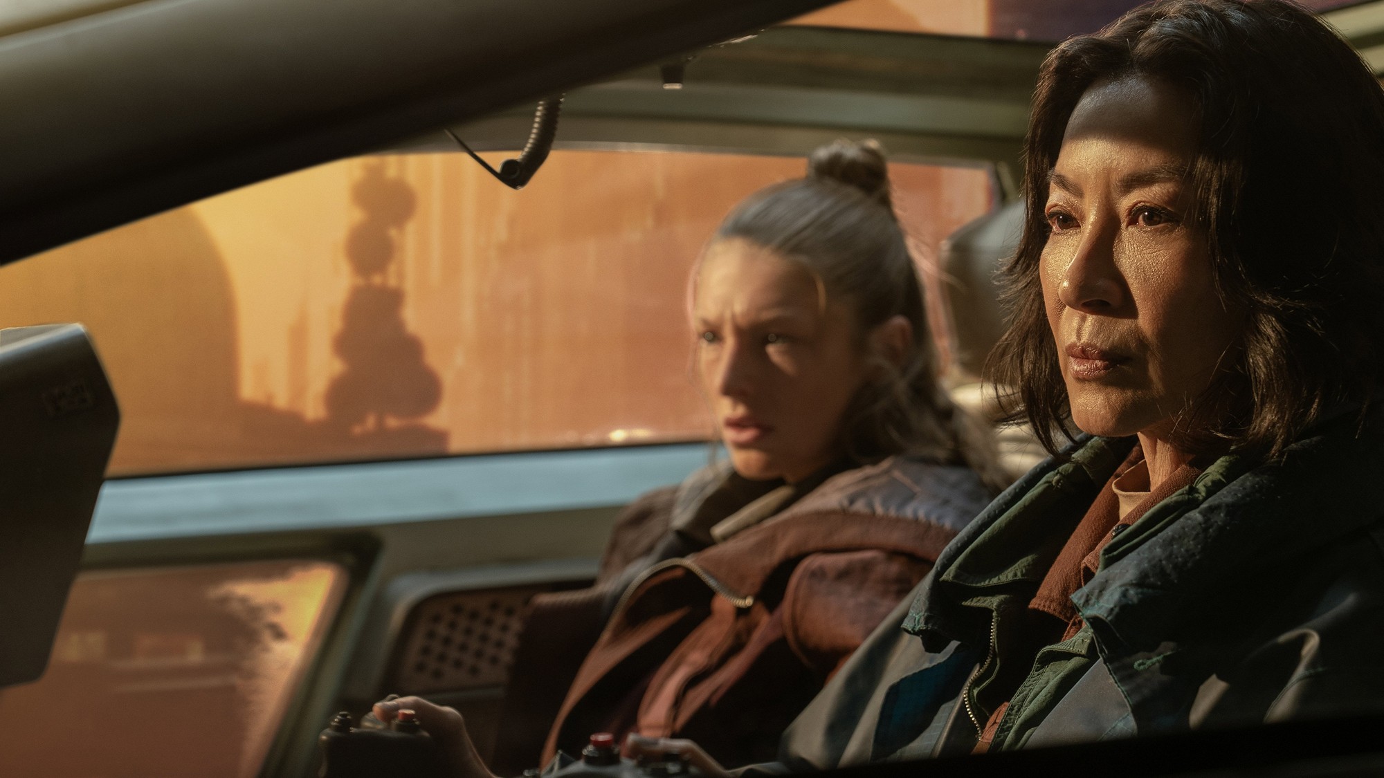 Michelle Yeoh y Hunter Schafer dentro de un vehículo con la ciudad futurista de fondo en Blade Runner 2099