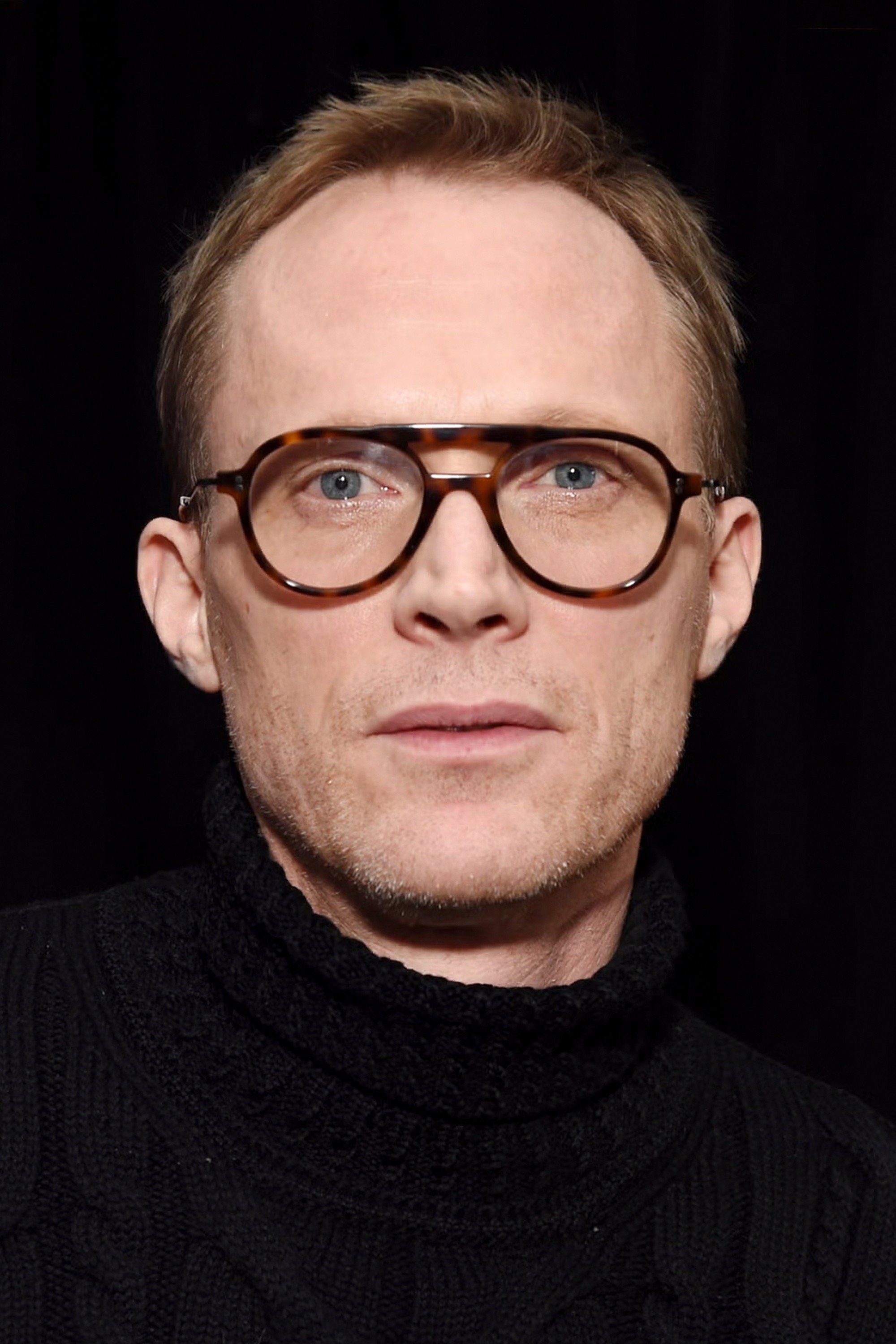 Retrato de Paul Bettany con lentes de montura carey y suéter negro de cuello alto