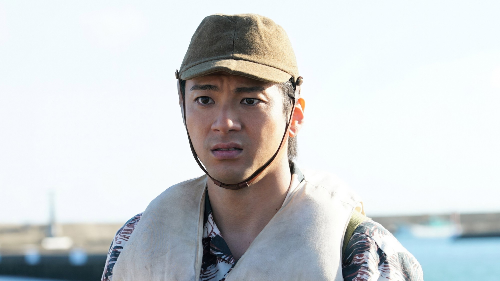 Un joven con gorra militar y chaleco salvavidas mira con angustia frente al mar en Godzilla Minus Zero