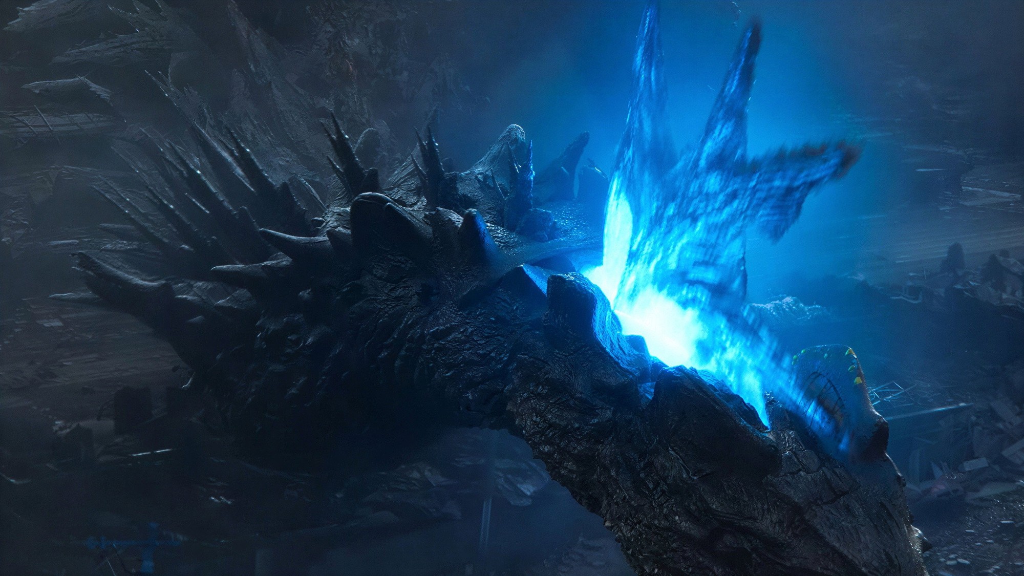 Las placas dorsales de Godzilla brillan con una intensa luz azul entre escombros y oscuridad