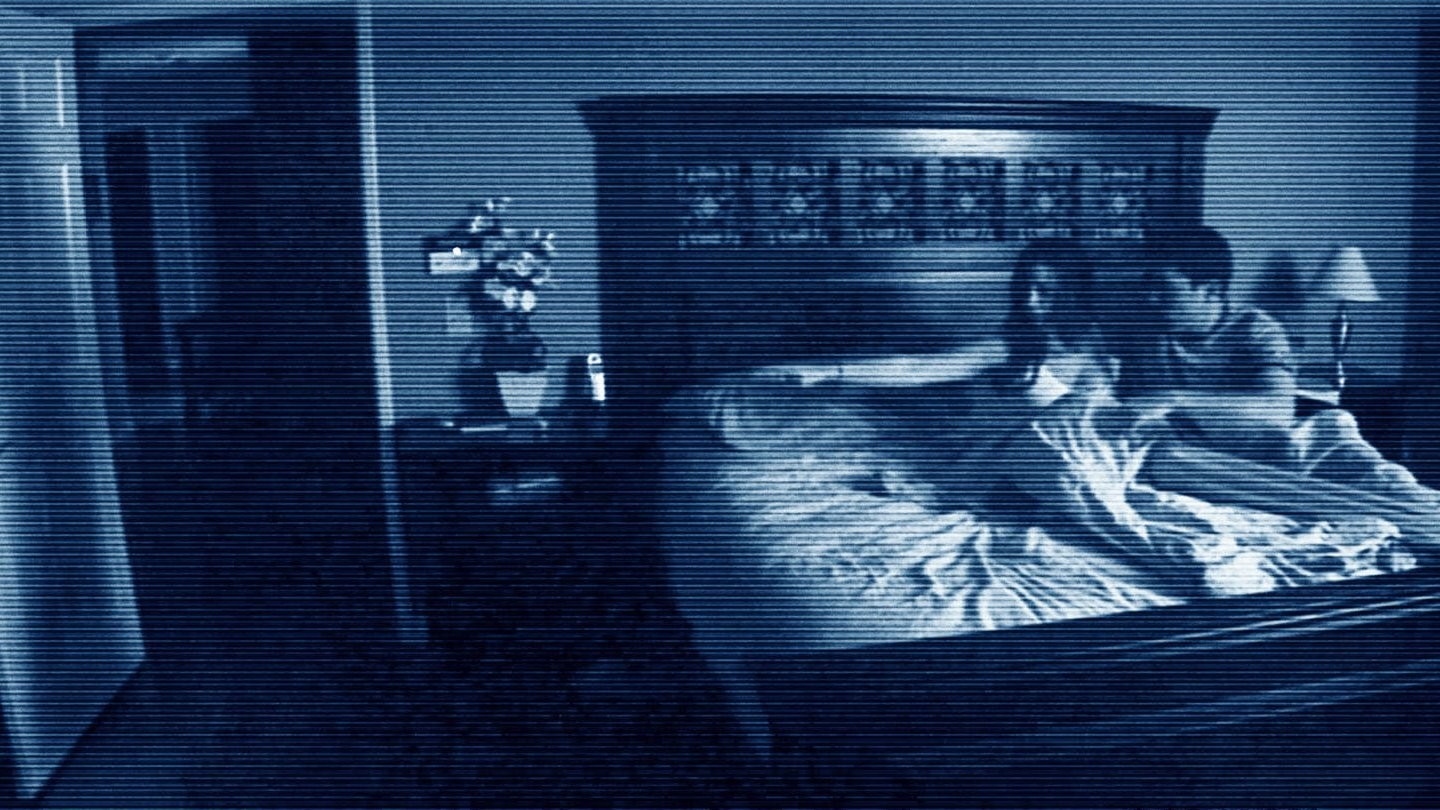 Una pareja sentada en la cama de su habitación a oscuras, captada por una cámara de visión nocturna en Paranormal Activity (2007)