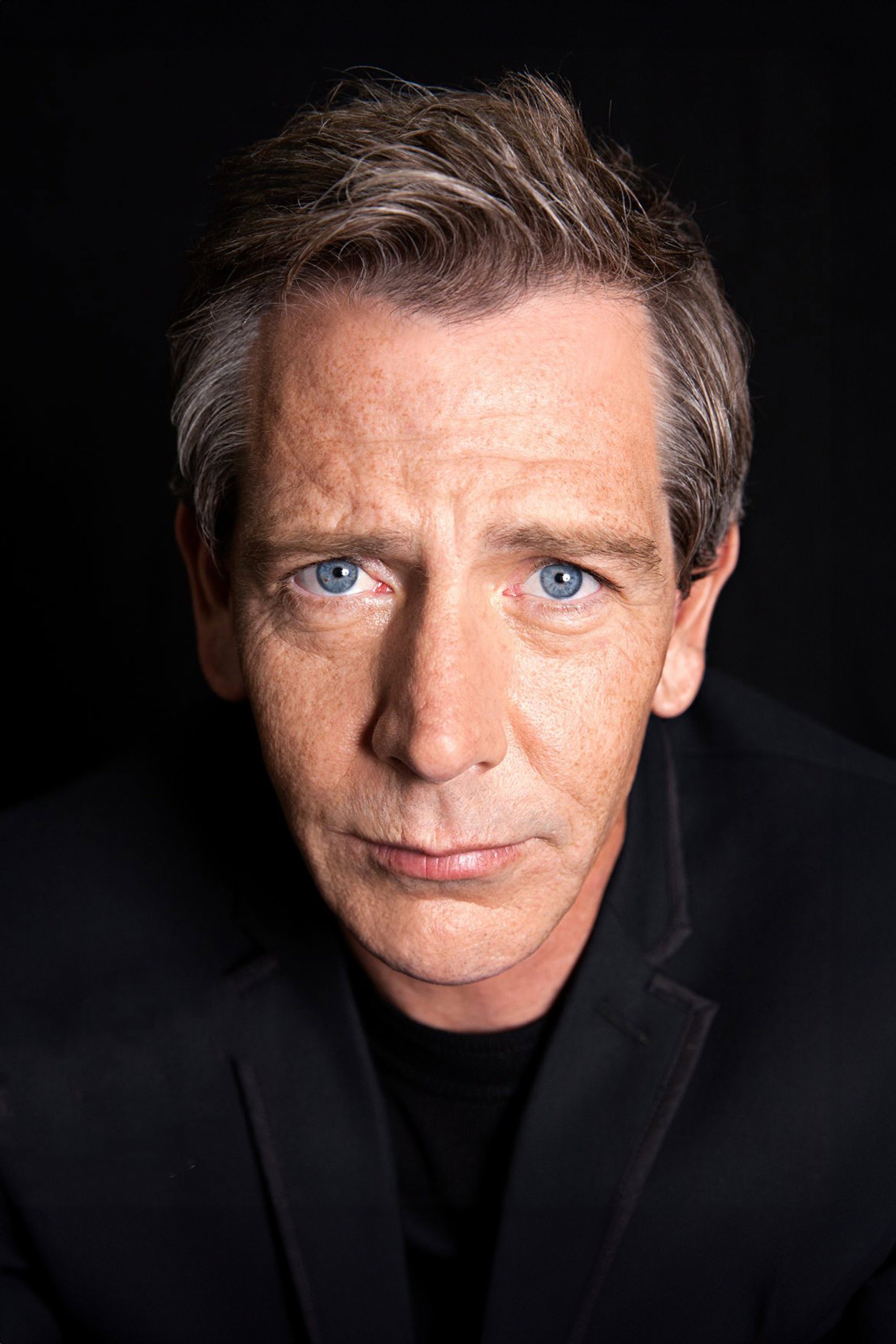 Retrato de Ben Mendelsohn con chaqueta oscura sobre fondo negro