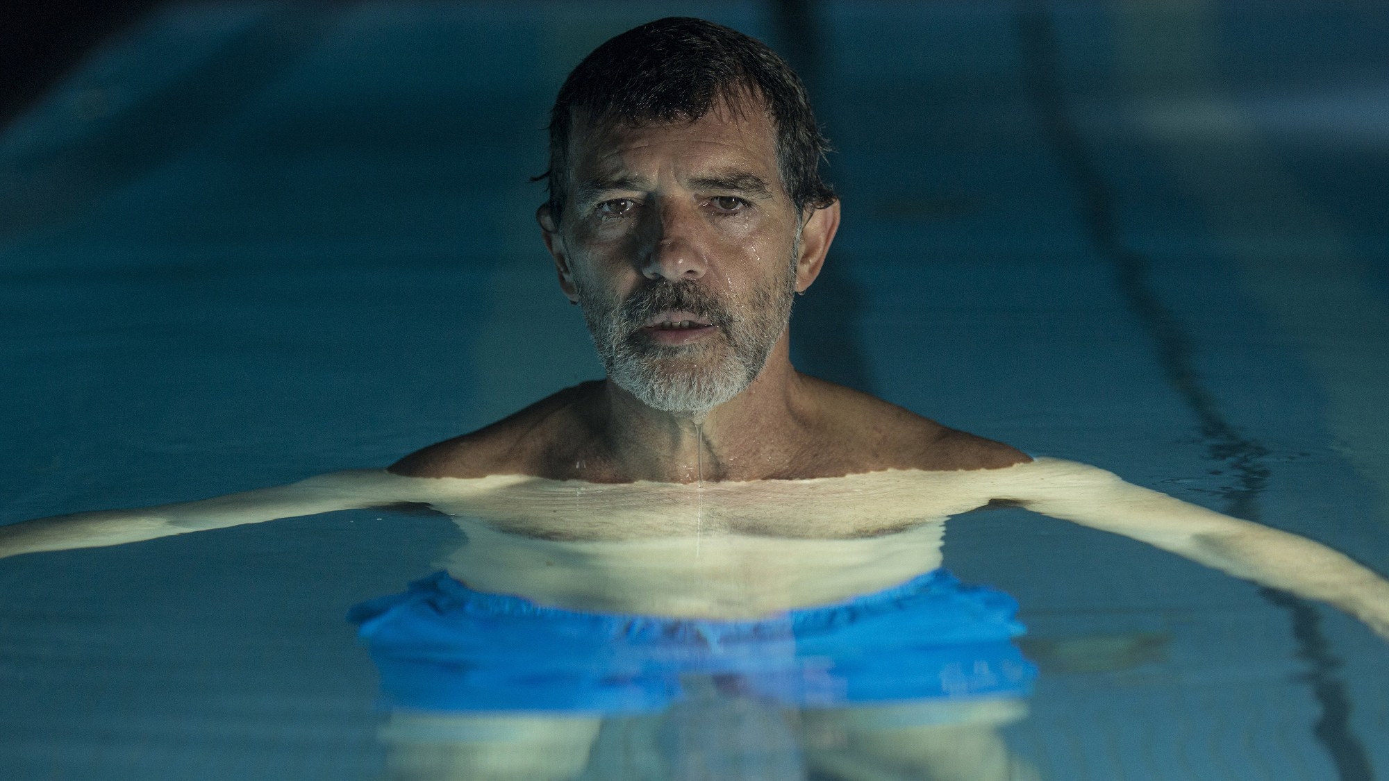 Antonio Banderas flota en una piscina iluminada de azul en una escena de Dolor y gloria