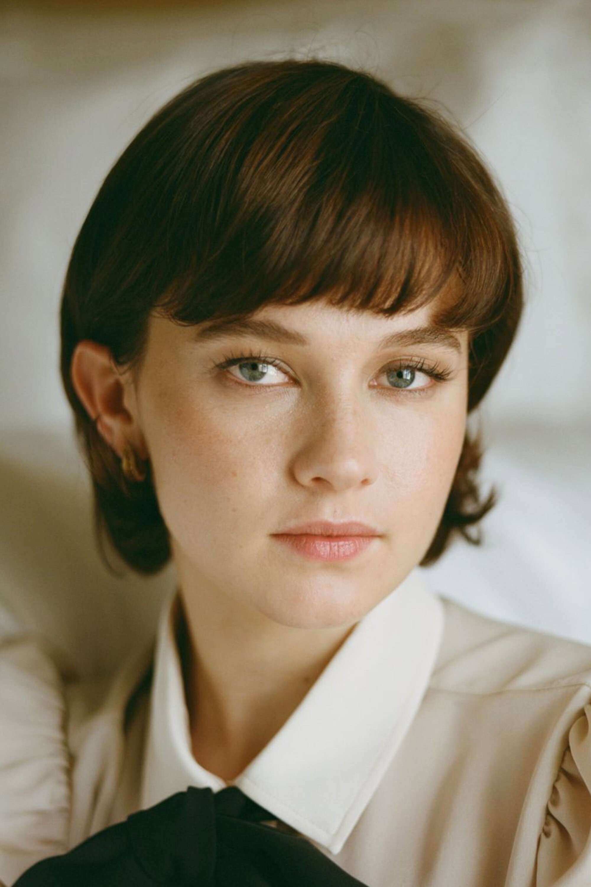 Retrato de la actriz Cailee Spaeny con flequillo y blusa de cuello blanco en luz cálida