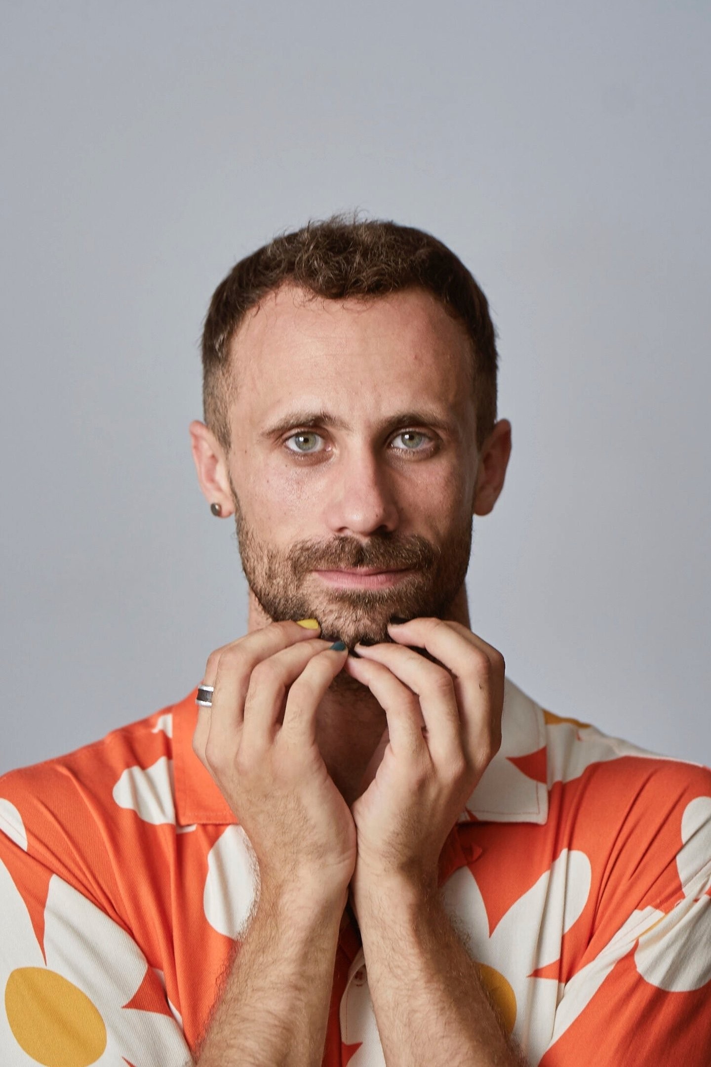 Oriol Pla, el Magistral Fermín de Pas en La Regenta, posa con las manos junto al rostro y una camisa naranja de flores