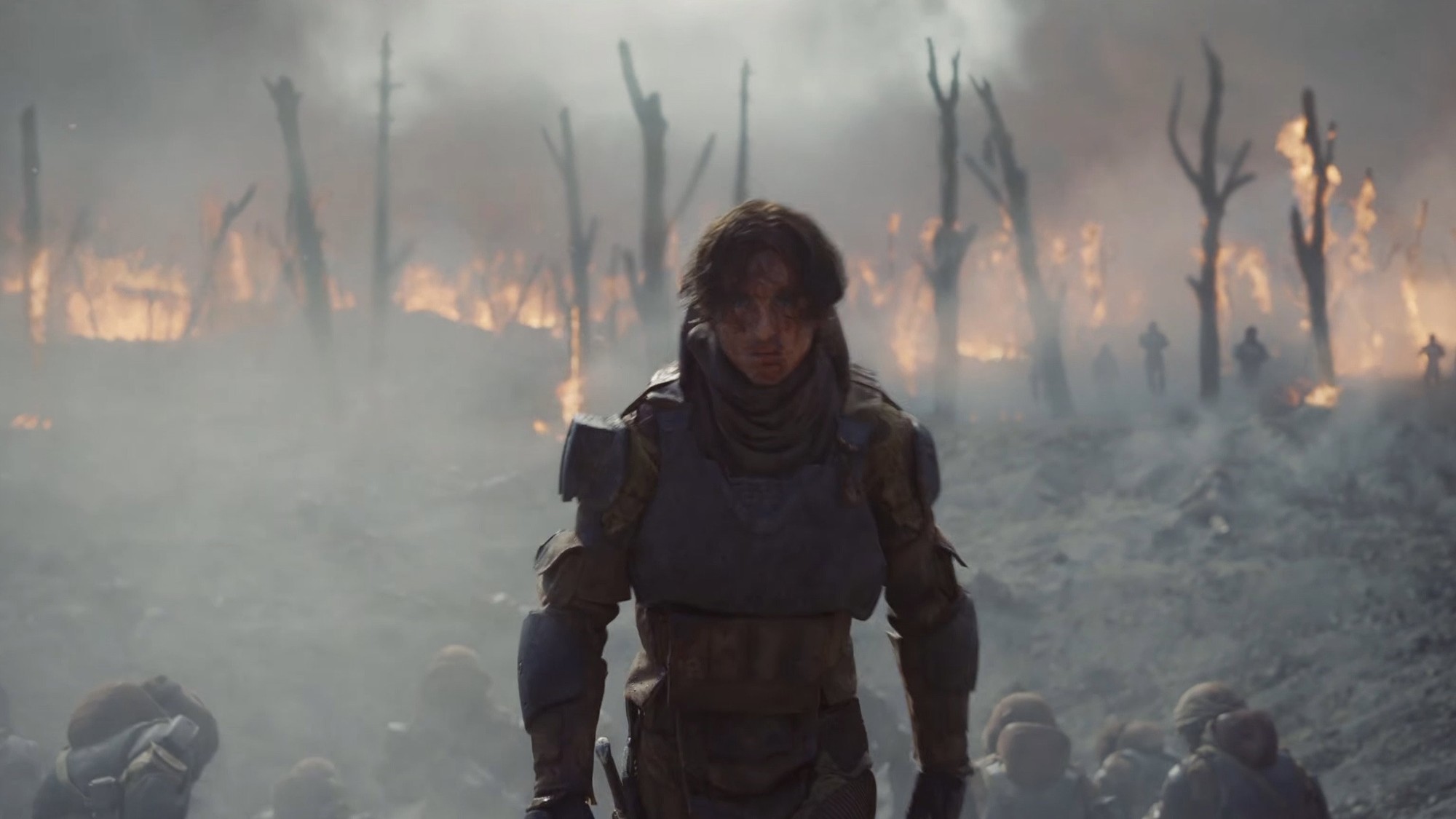 Paul Atreides con armadura avanza entre el humo y los árboles en llamas de un campo de batalla