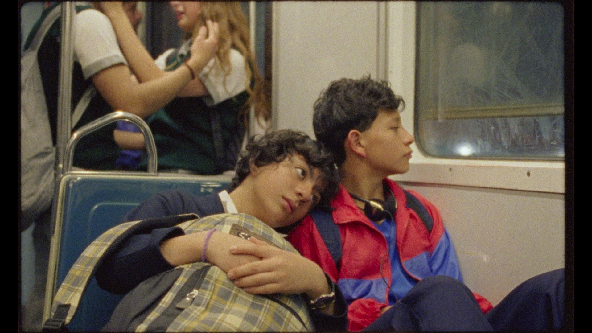 Dos niños con uniforme escolar viajan en el metro y uno recarga la cabeza en el hombro del otro