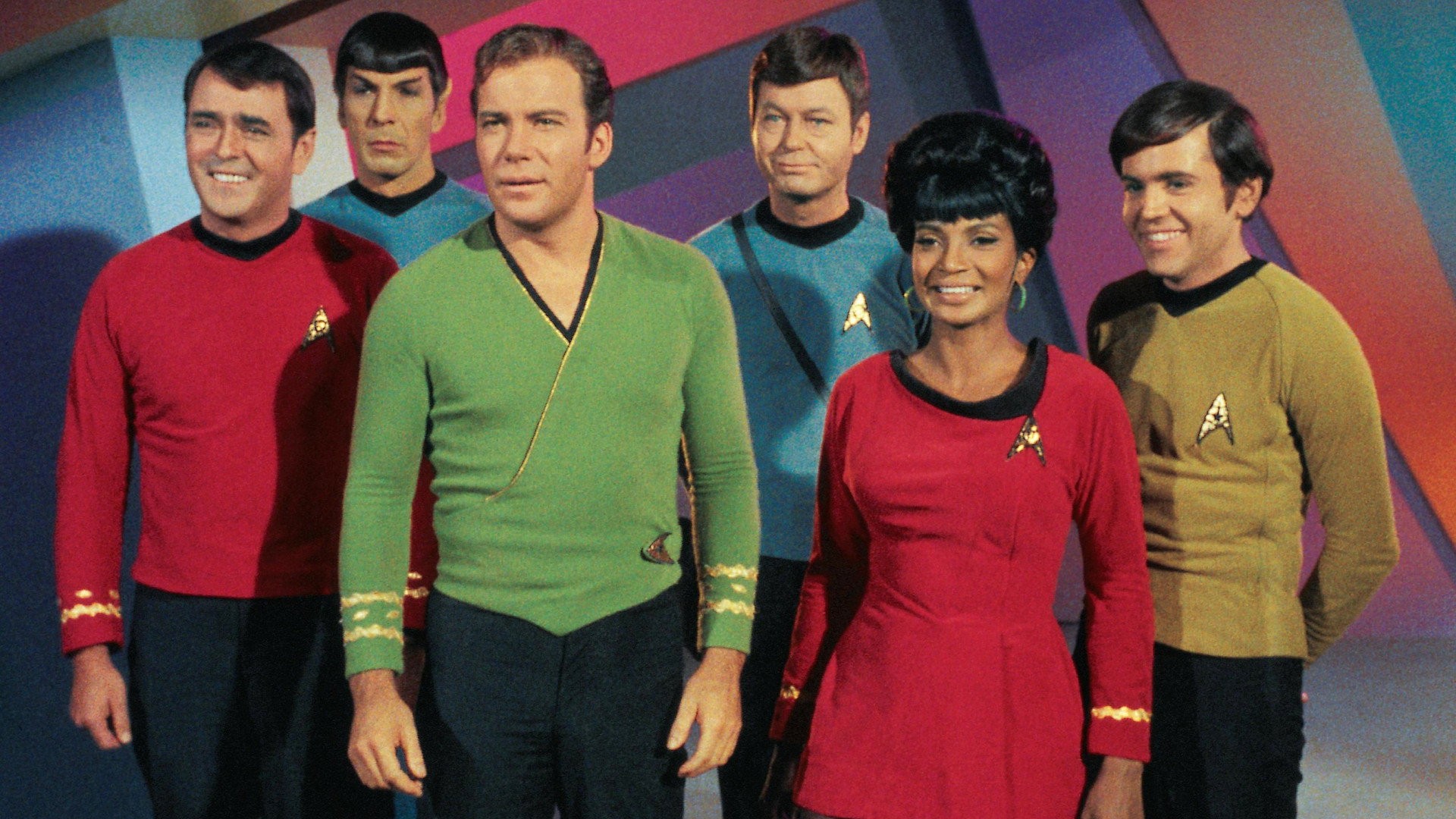 Walter Koenig sonríe junto a William Shatner, Leonard Nimoy, DeForest Kelley, Nichelle Nichols y James Doohan con los uniformes de la serie original de Star Trek