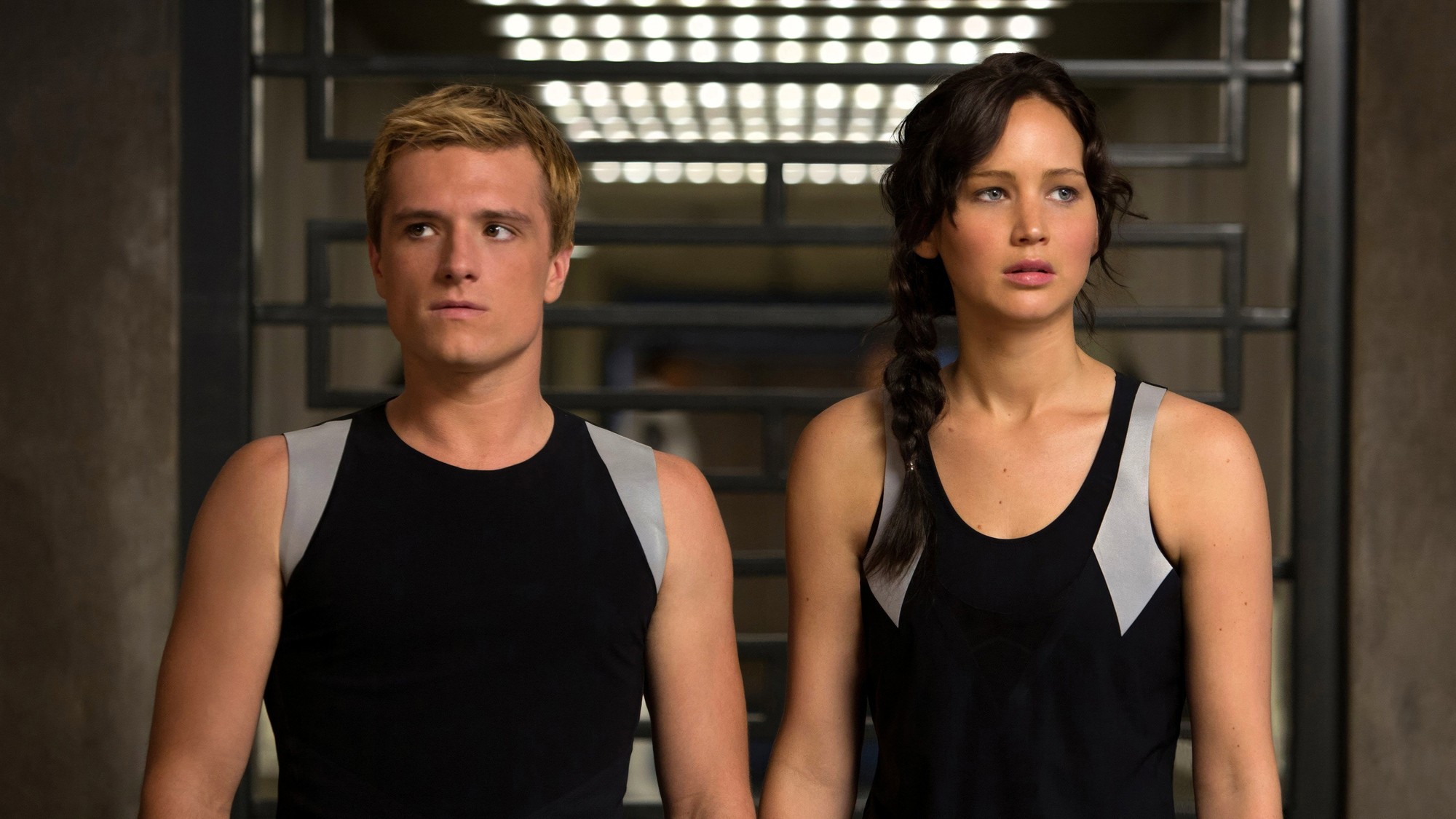 Josh Hutcherson como Peeta Mellark y Jennifer Lawrence como Katniss Everdeen, de pie lado a lado con camisetas negras de entrenamiento en Los Juegos del Hambre: En llamas