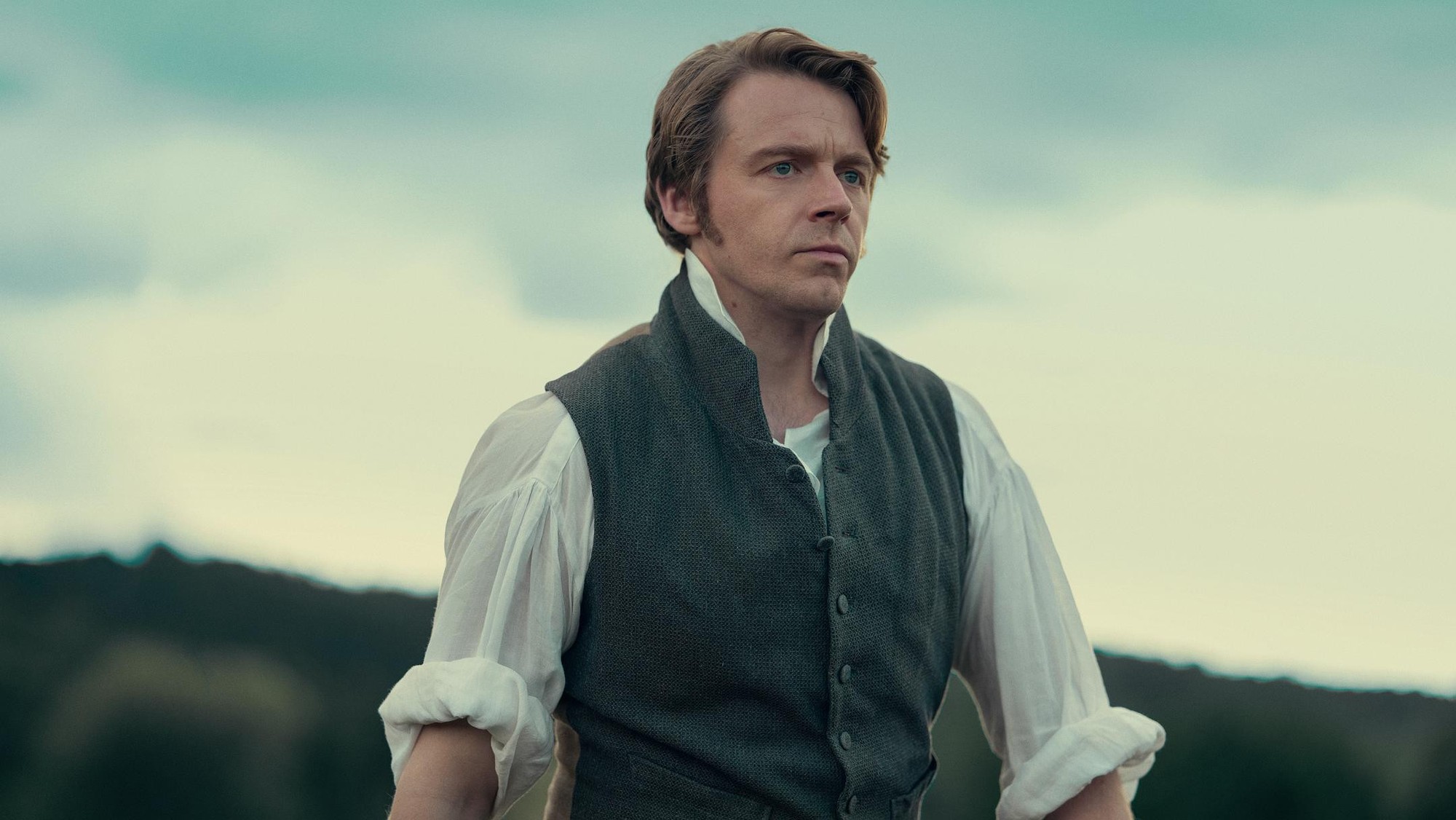Jack Lowden como el señor Darcy, de chaleco y camisa blanca, en el campo inglés