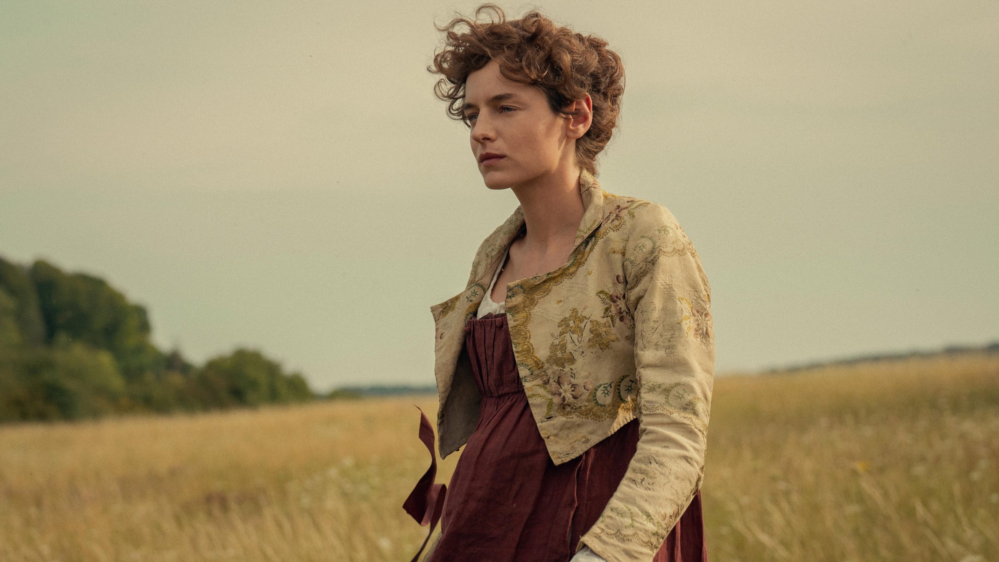 Emma Corrin como Elizabeth Bennet, de pie en un campo de pasto dorado