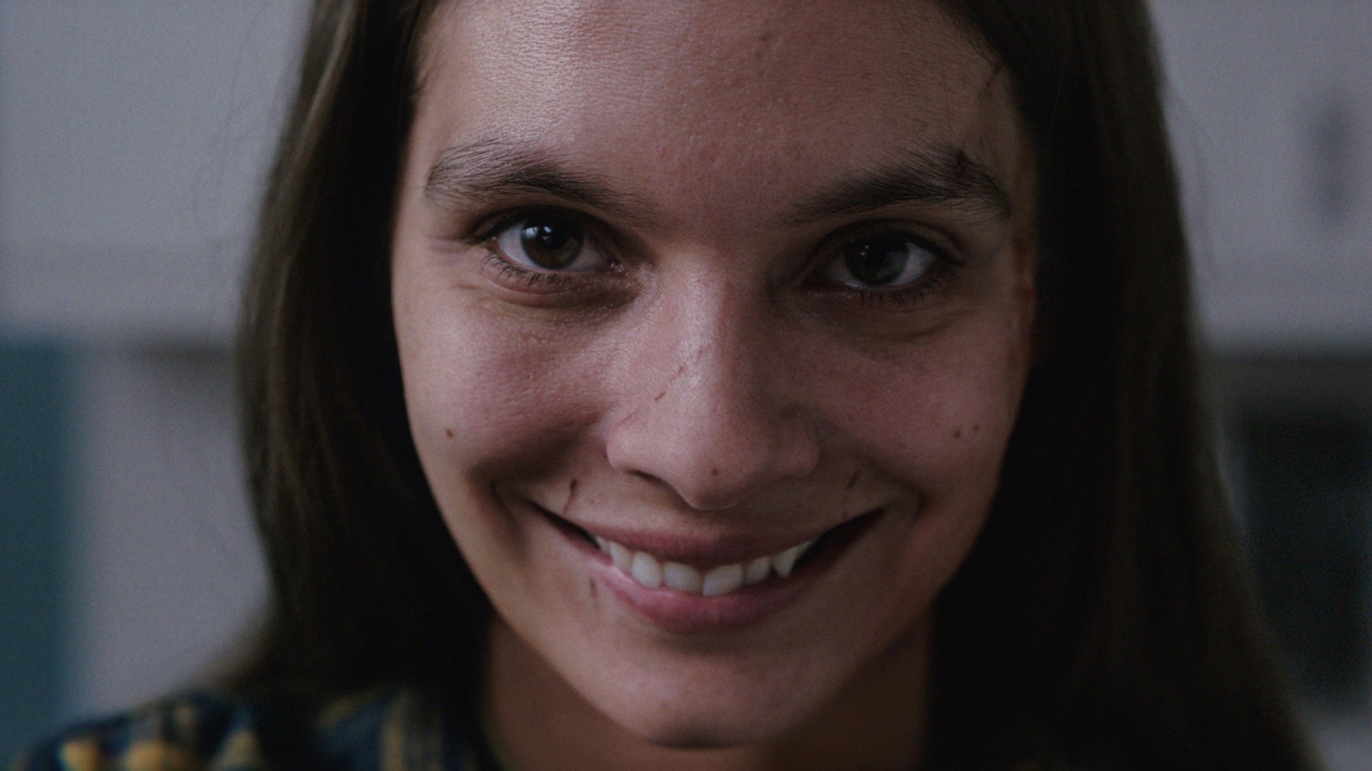 Primer plano de una mujer con una sonrisa forzada y perturbadora que mira fijamente a la cámara en Smile (2022)