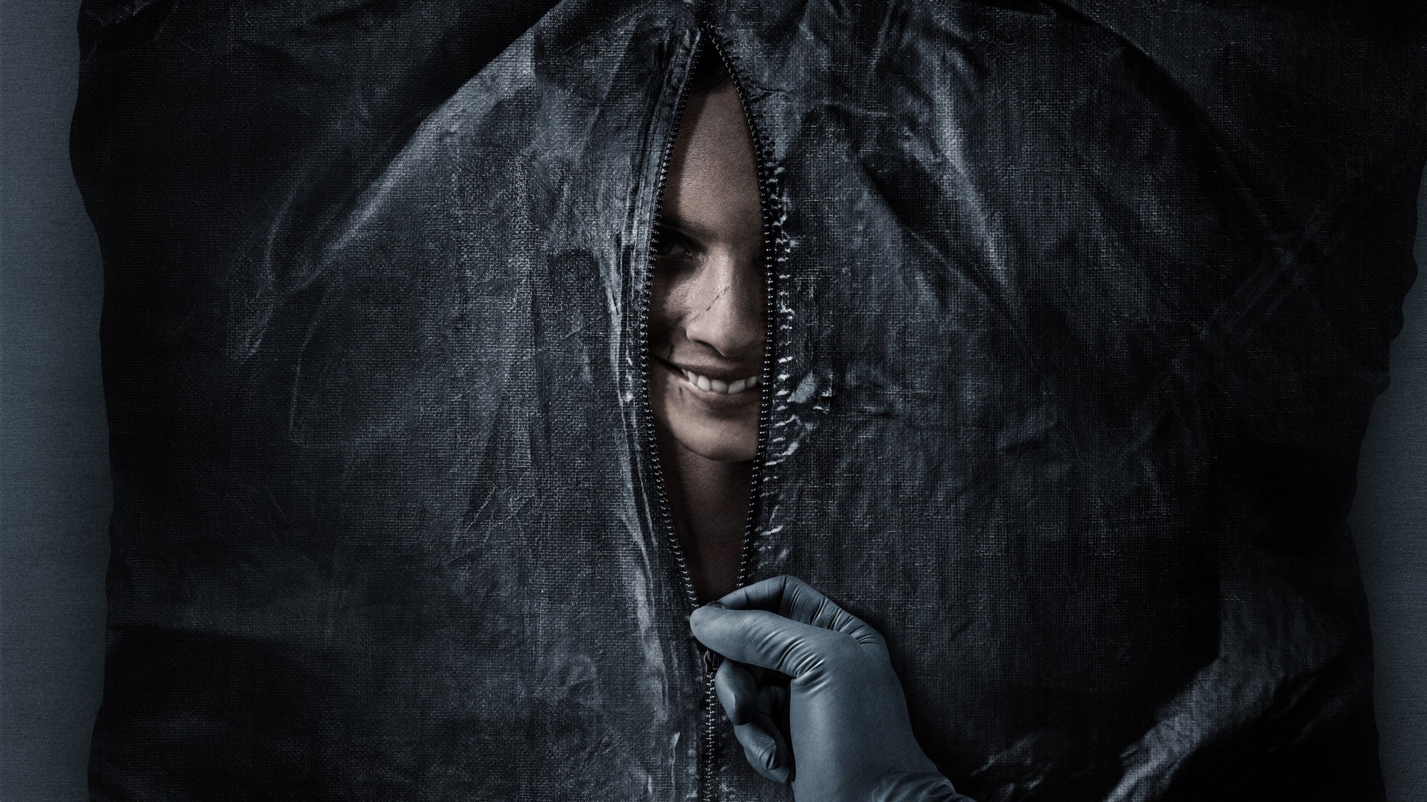 Una mano con guante de látex abre la cremallera de una bolsa negra y deja ver un rostro sonriente, imagen de Smile (2022)