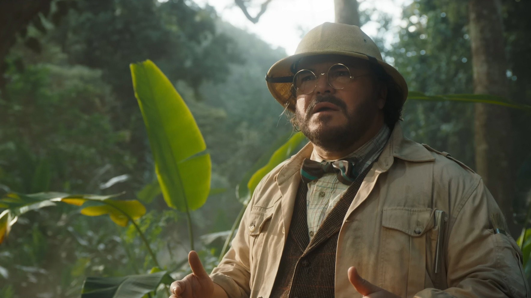 El profesor Shelly Oberon, con sombrero de explorador y lentes redondos, gesticula en medio de una vegetación tropical