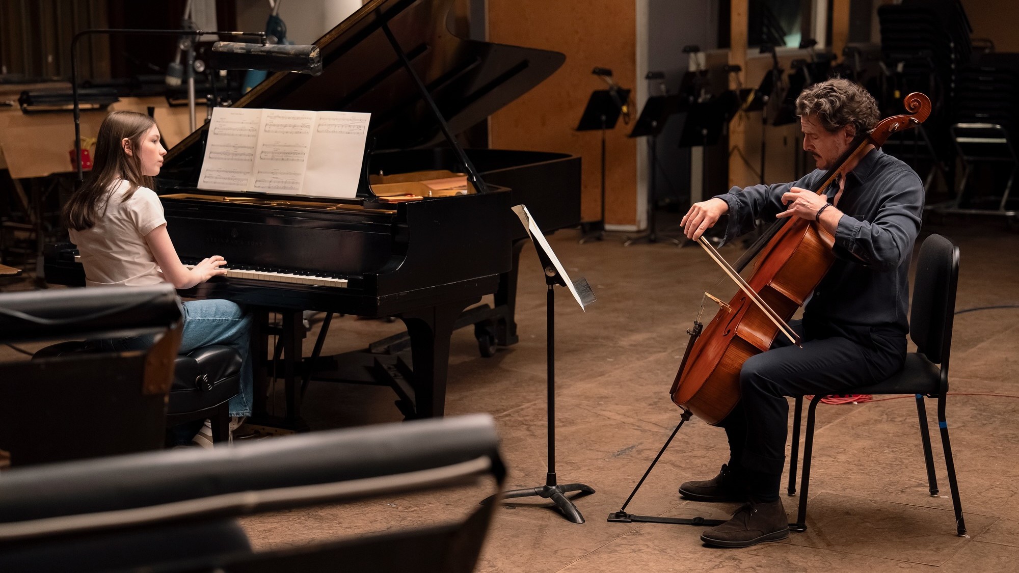 Pedro Pascal como Alex Serian toca el violonchelo junto a una joven pianista en un estudio de grabación