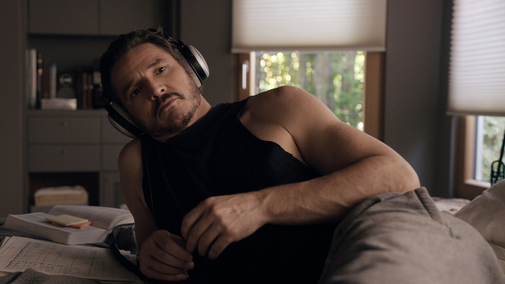 Pedro Pascal recostado en la cama con audífonos grandes y partituras a su lado