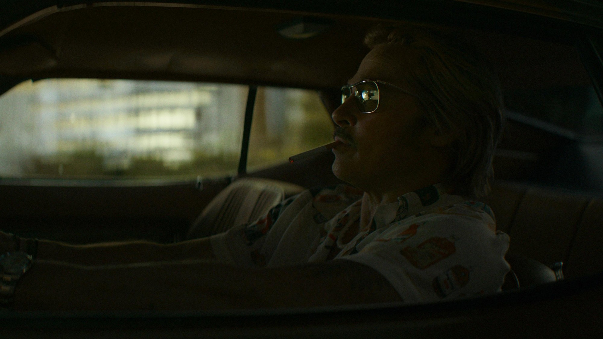 Brad Pitt como Cliff Booth, con gafas y un cigarrillo en la boca, conduce de noche en Las nuevas desventuras de Cliff Booth